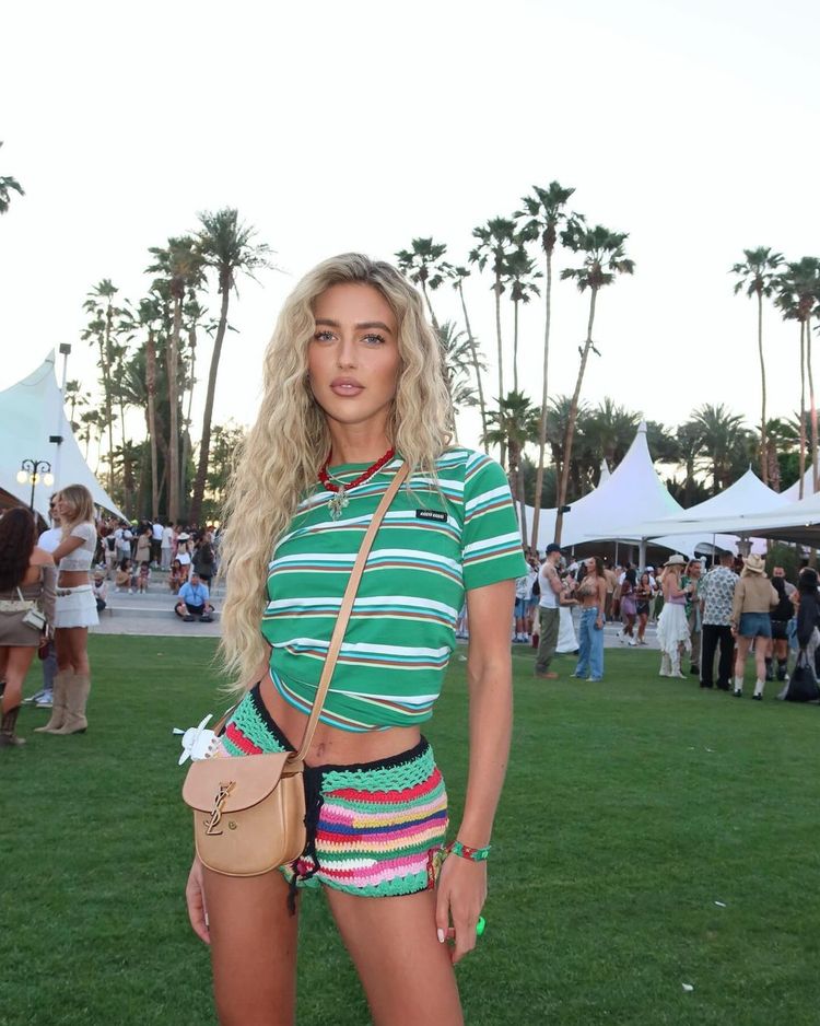 Emili Sindlev wears crochet booty shorts, a striped top, and red cowboy boots at Coachella 2024