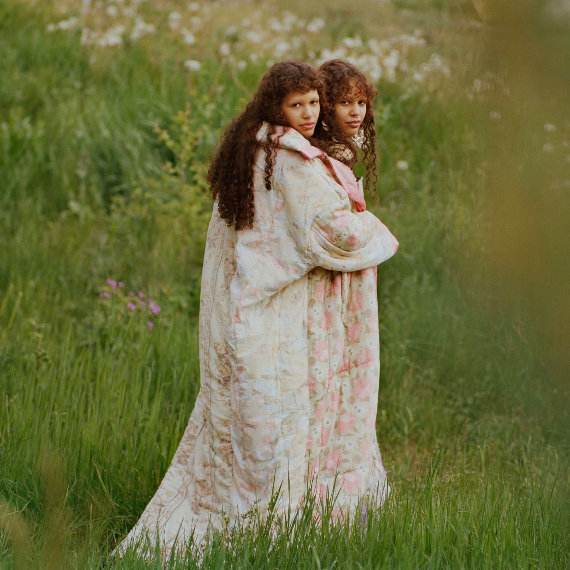 Two models stand in a field wearing quilted rose-printed long coats