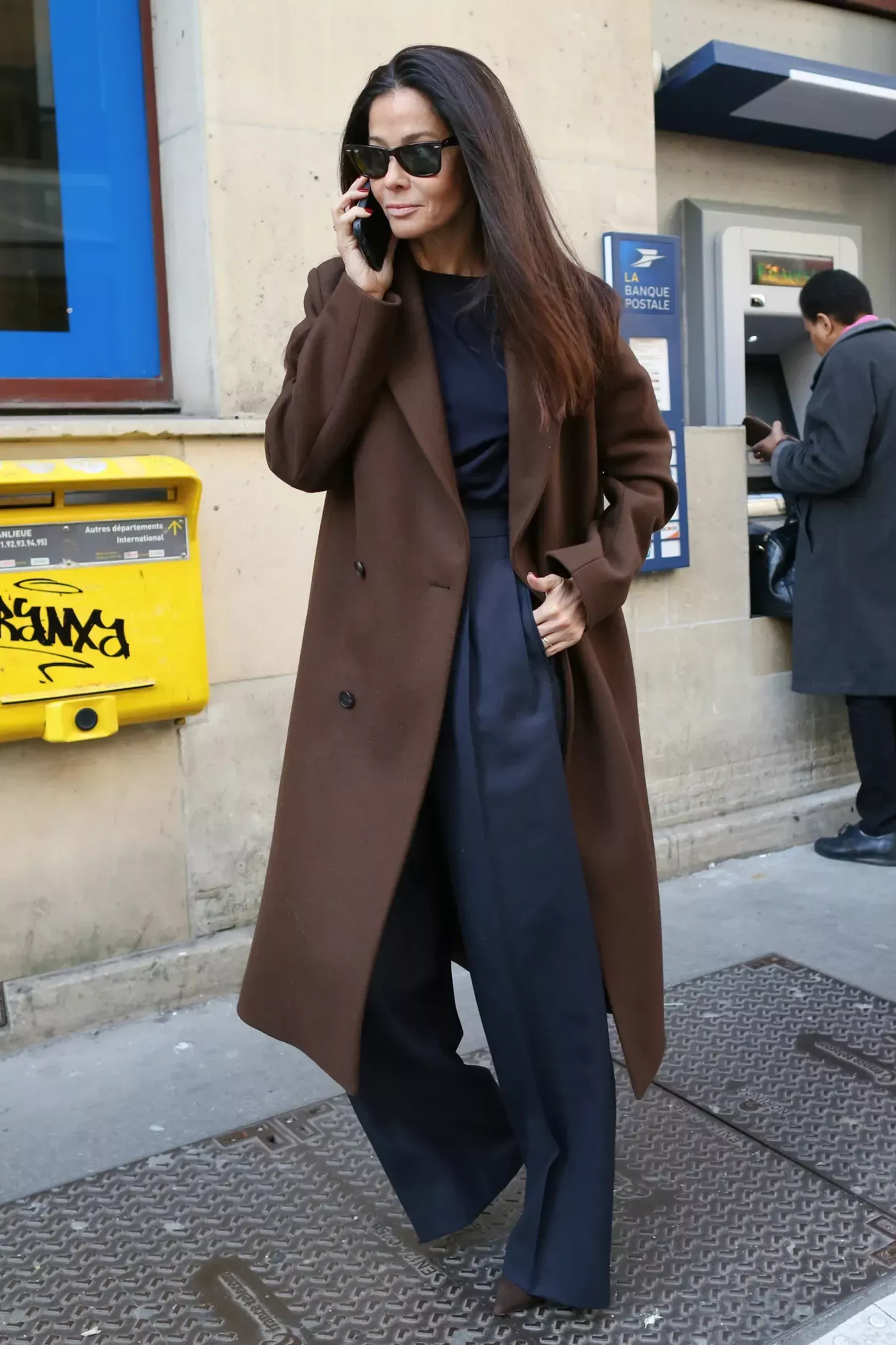 Paris Fashion Week guest wears brown coat over black top and pants 