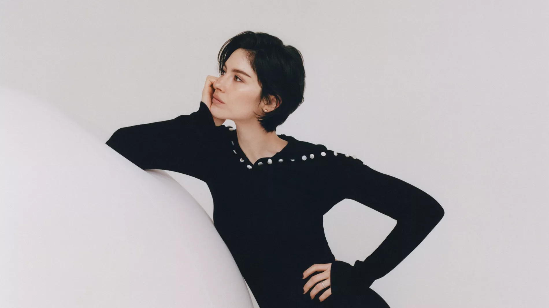Gracie Abrams poses in a black knitted dress on a white soundstage for the Coco Mademoiselle Cursh Absolu campaign