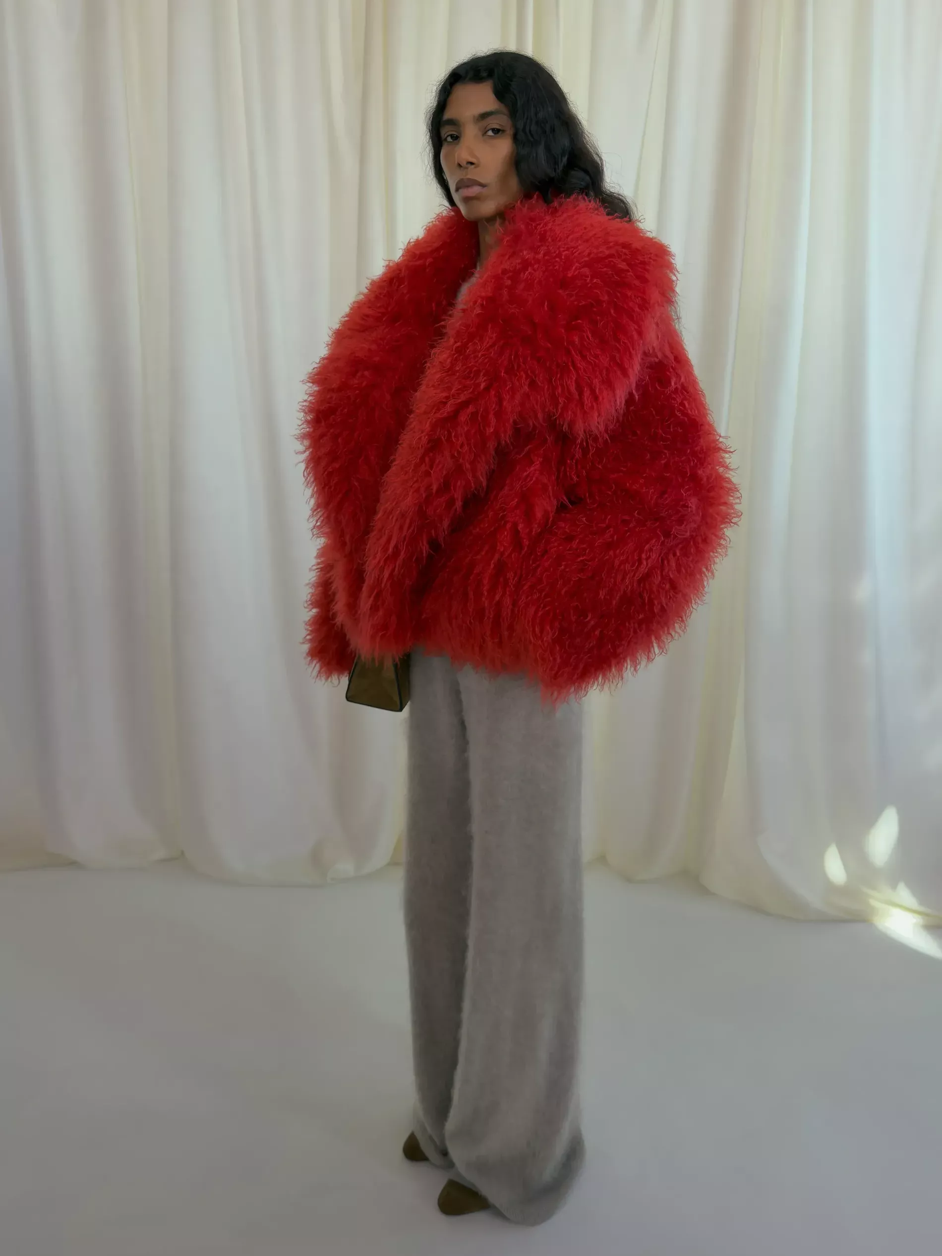 A model at Nanushka fall 2026 wears a red faux fur jacket and grey knitted sweatpants
