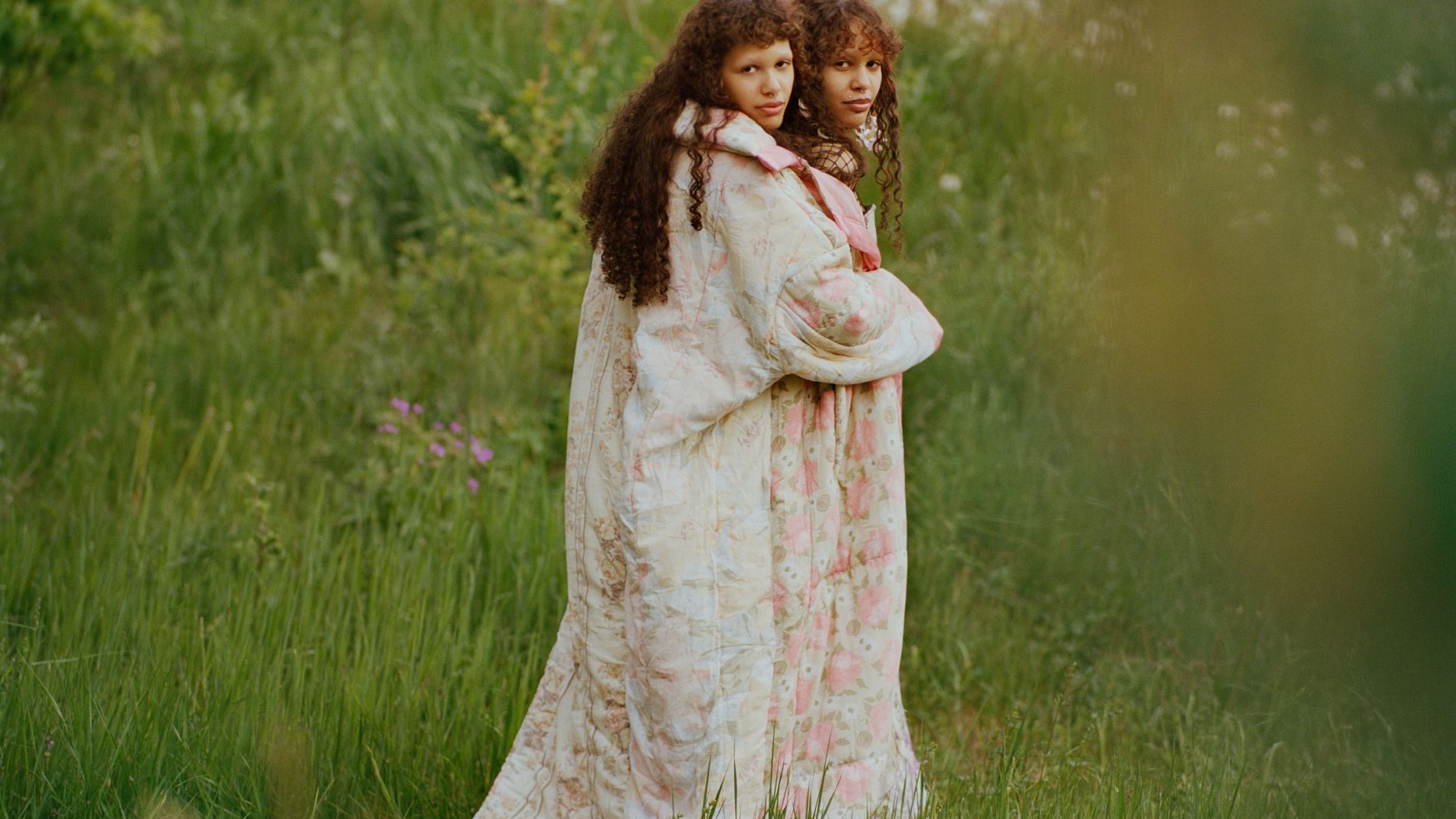 Two models stand in a field wearing quilted rose-printed long coats
