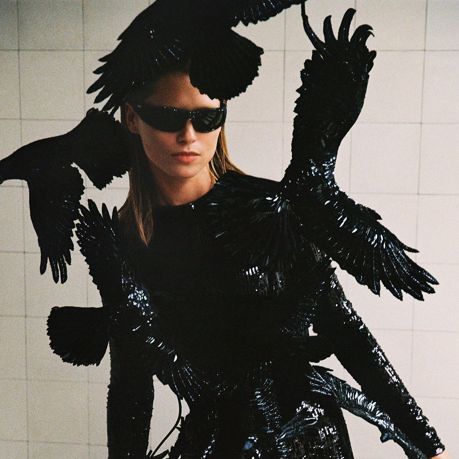 Model in black catsuit with crows in a white tiled room