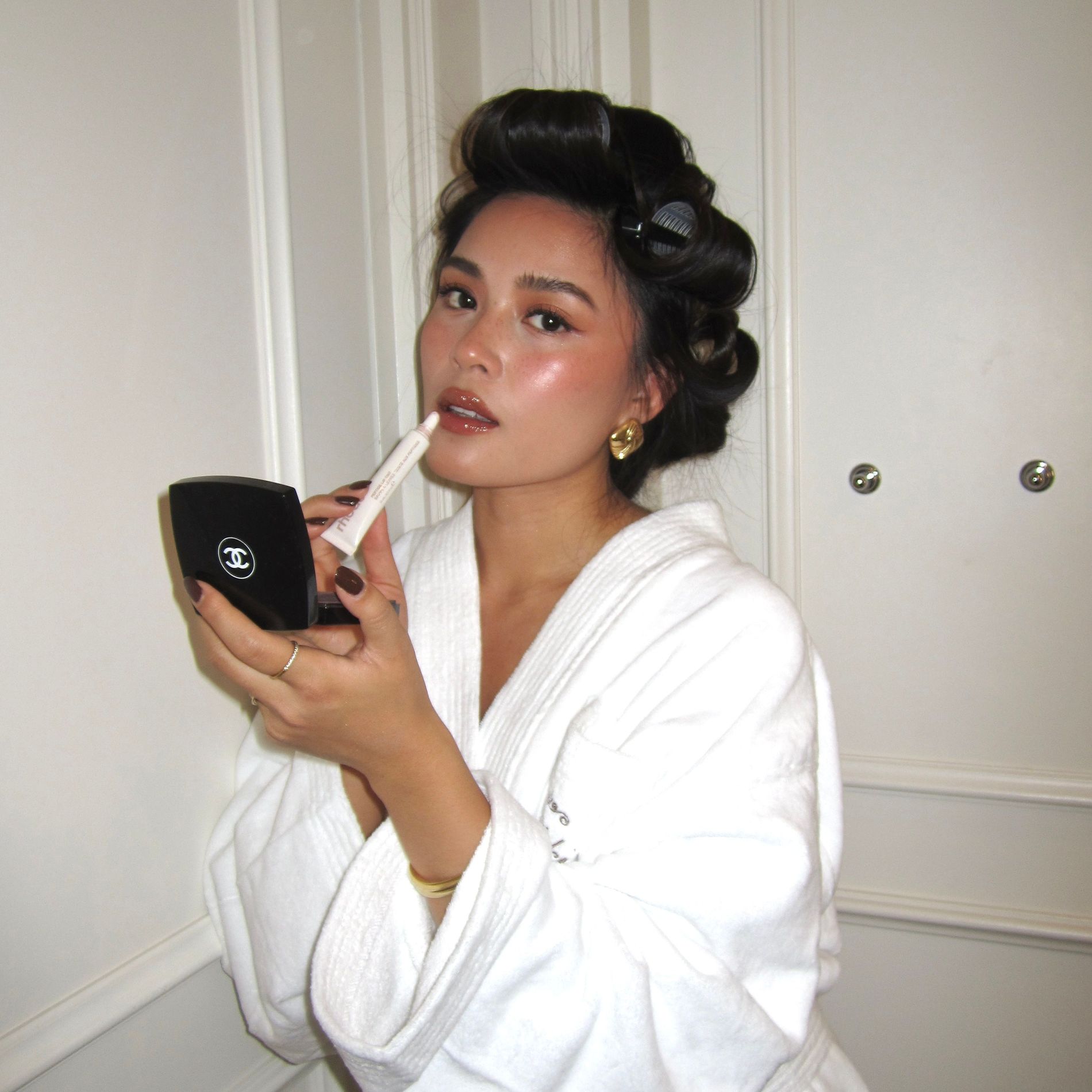 Tsutsumi Hoang poses with her hair in rollers, glowing makeup and a robe while applying lipstick in a Chanel mirror