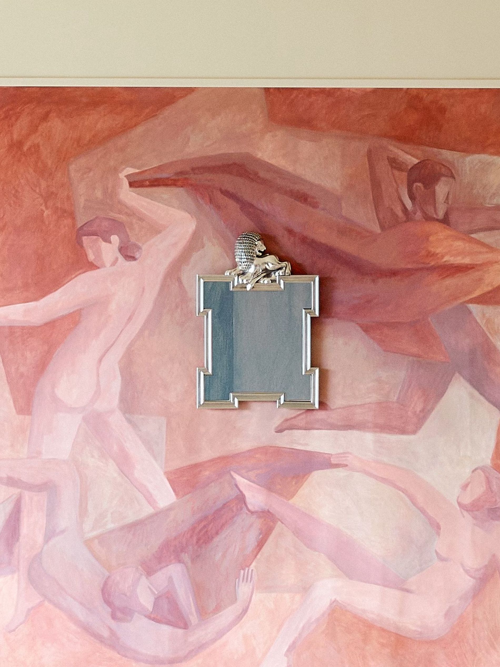A red terracotta wall painted with naked people dancing and a silver mirror with a lion on the frame from Svenskt tenn Fall' 26