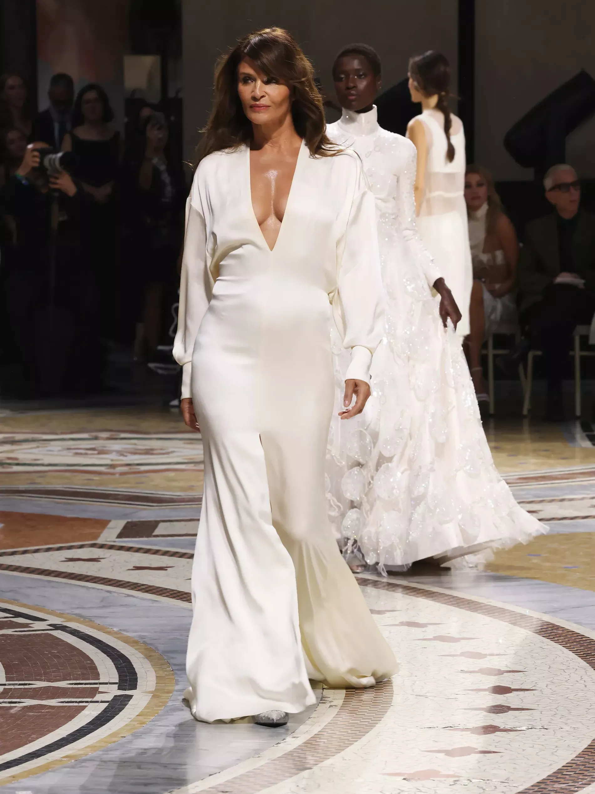 Helena Christensen Helena Christensen appears on the runway in an elegant, custom-made ivory silk gown featuring a deep V-neckline, Brunello Cucinelli custom creation, in Galleria Vittorio Emanuele II, Milan fashion week