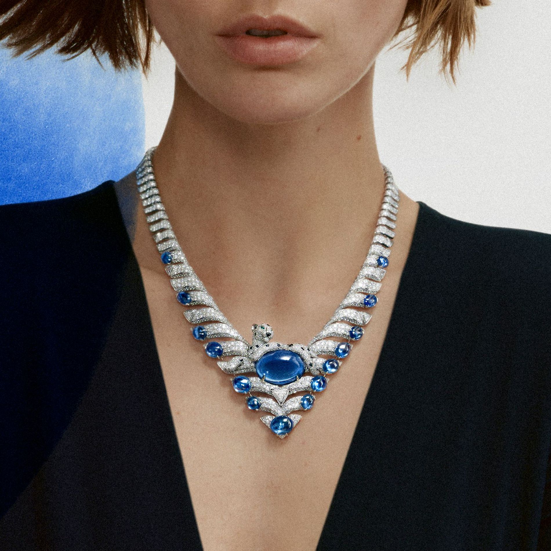 Model in black wears a necklace from Cartier high jewellery against a white background with a blue swipe of paint