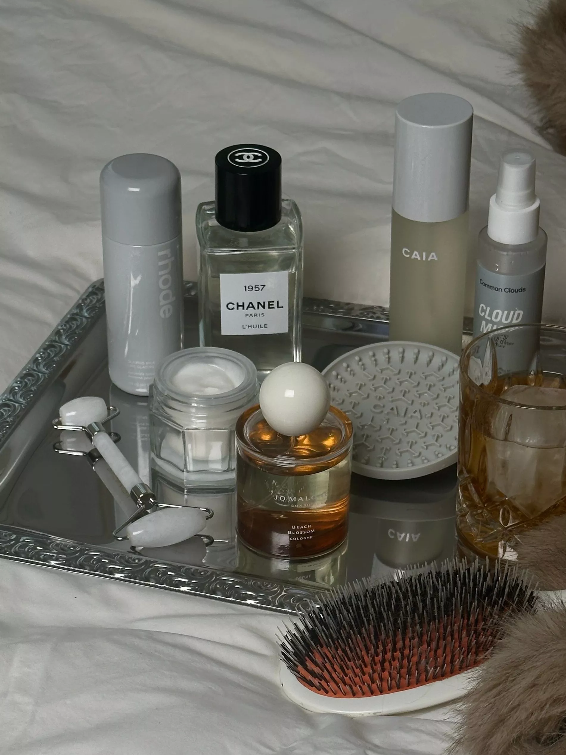 A collection of beauty items upon a silver tray on white sheets 