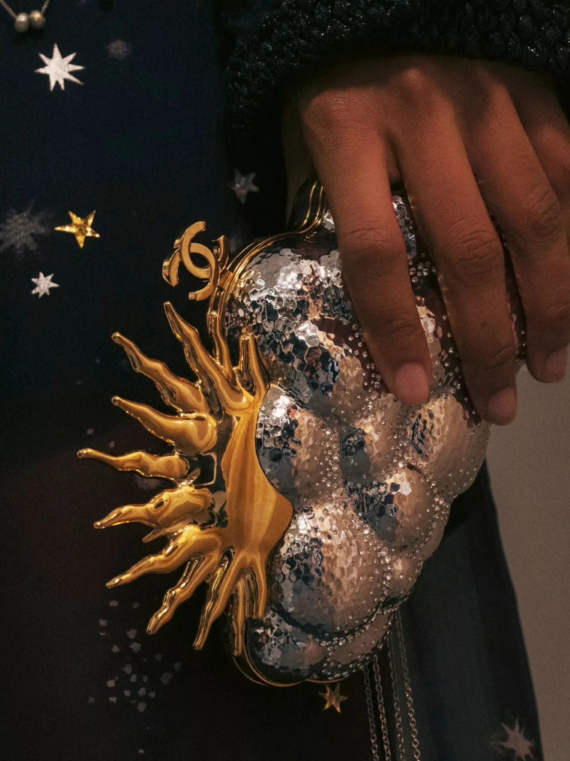 A close-up of a Chanel SS27 clutch in gold and silver, shaped like a cloud and sun