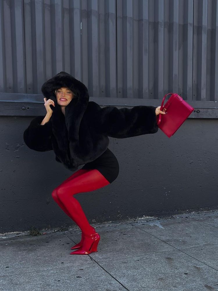 Elsa Hosk wears a faux fur jacket, a black mini dress and red stockings