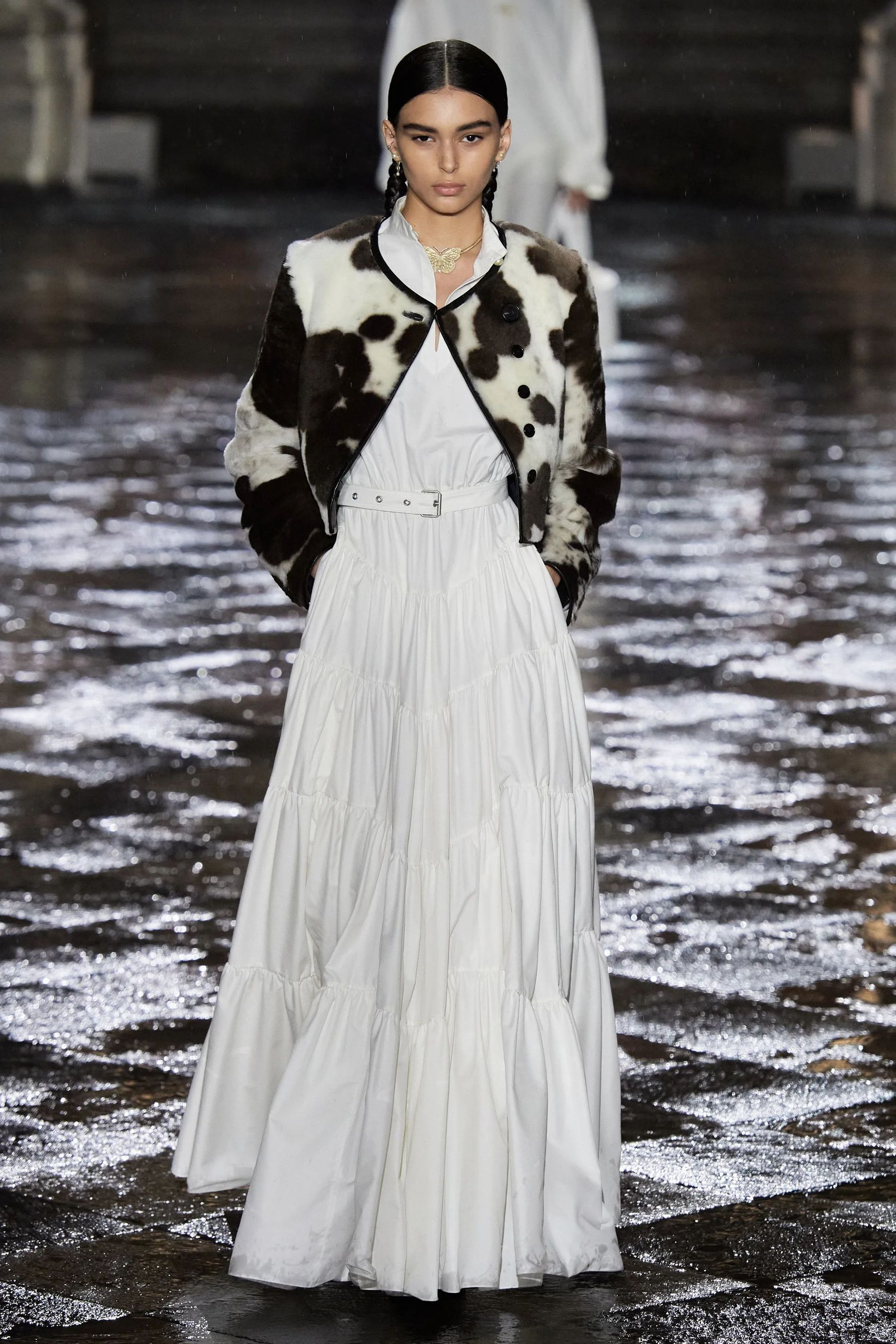 Model wearing a cropped cow print jacket over a tiered white prairie dress at Dior Cruise 2024