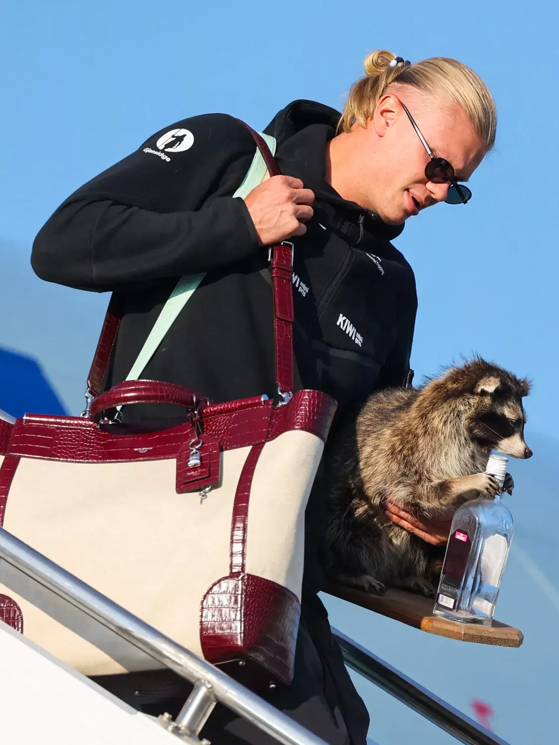 Erling Haaland stepping out of the plane in sunglasses wearing a big Dolce & Gabbana Sicily Tote Bag and holding a racoon in his left hand