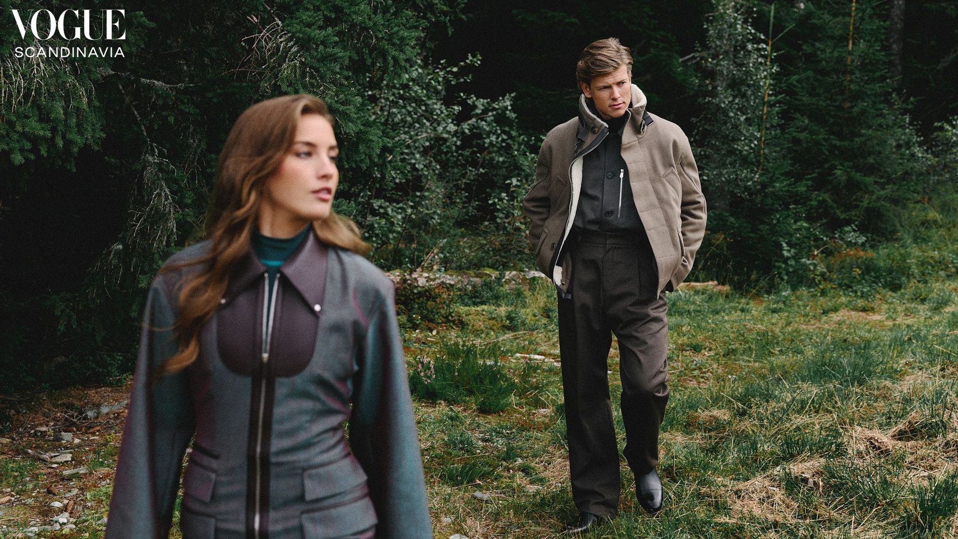 Klæbo and Døsvik stand against a forrest background. She wears an Hermès set, and he wears brown trousers, and beige jacket