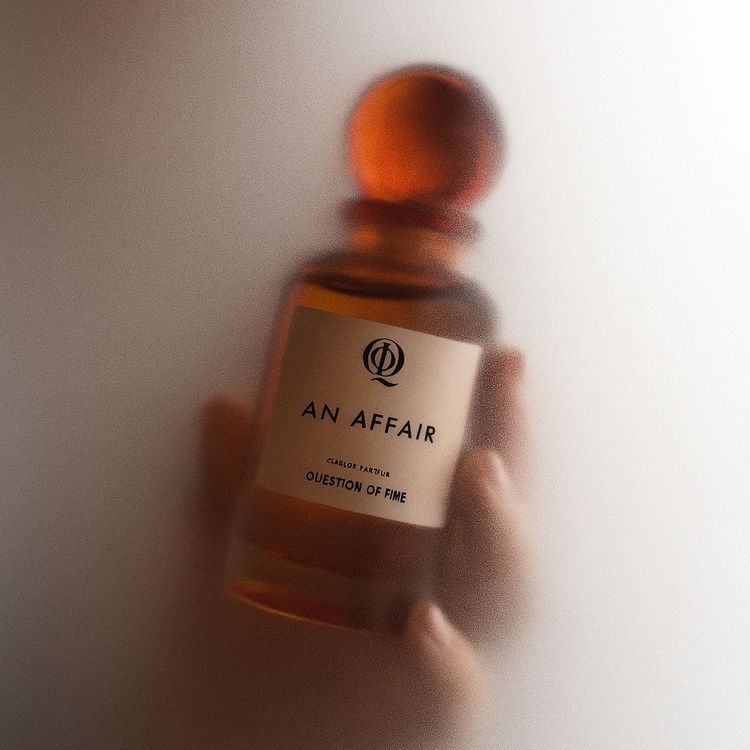 QOT's perfume 'An Affair' held in hand and surrounded by steam