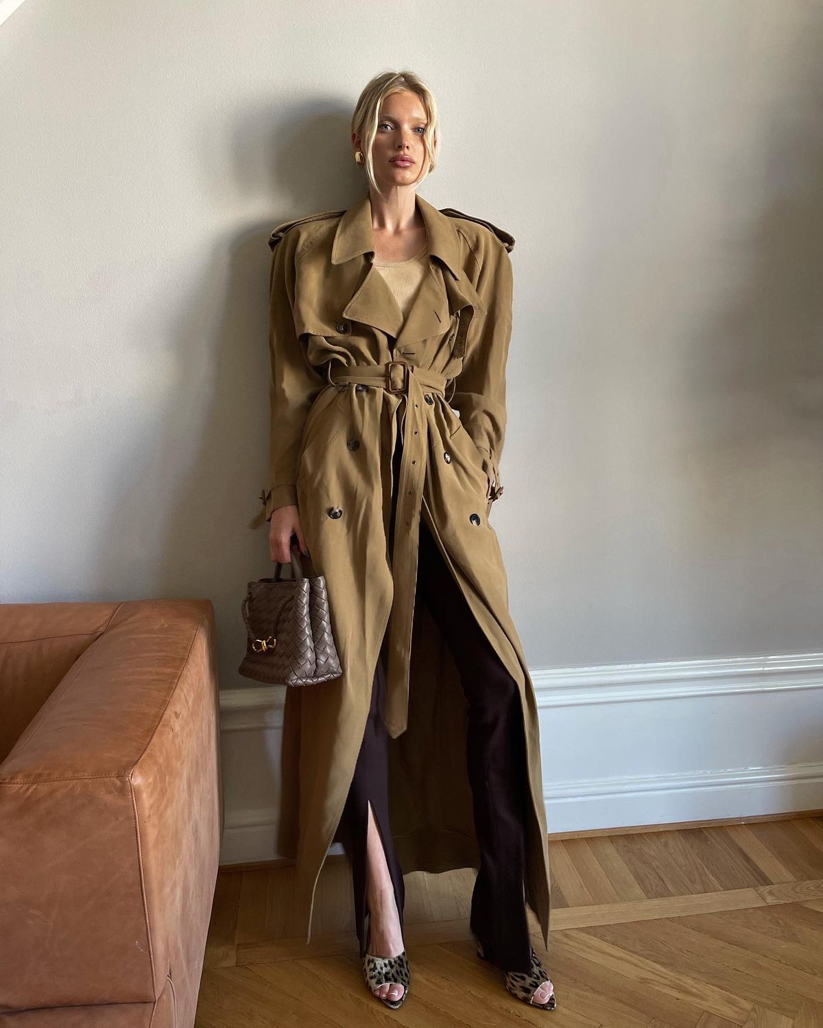 Elsa Hosk wears double-breasted trench coat by Saint Laurent, clip-on vintage earrings by Saint Laurent, and stretchy brown The Attico trousers