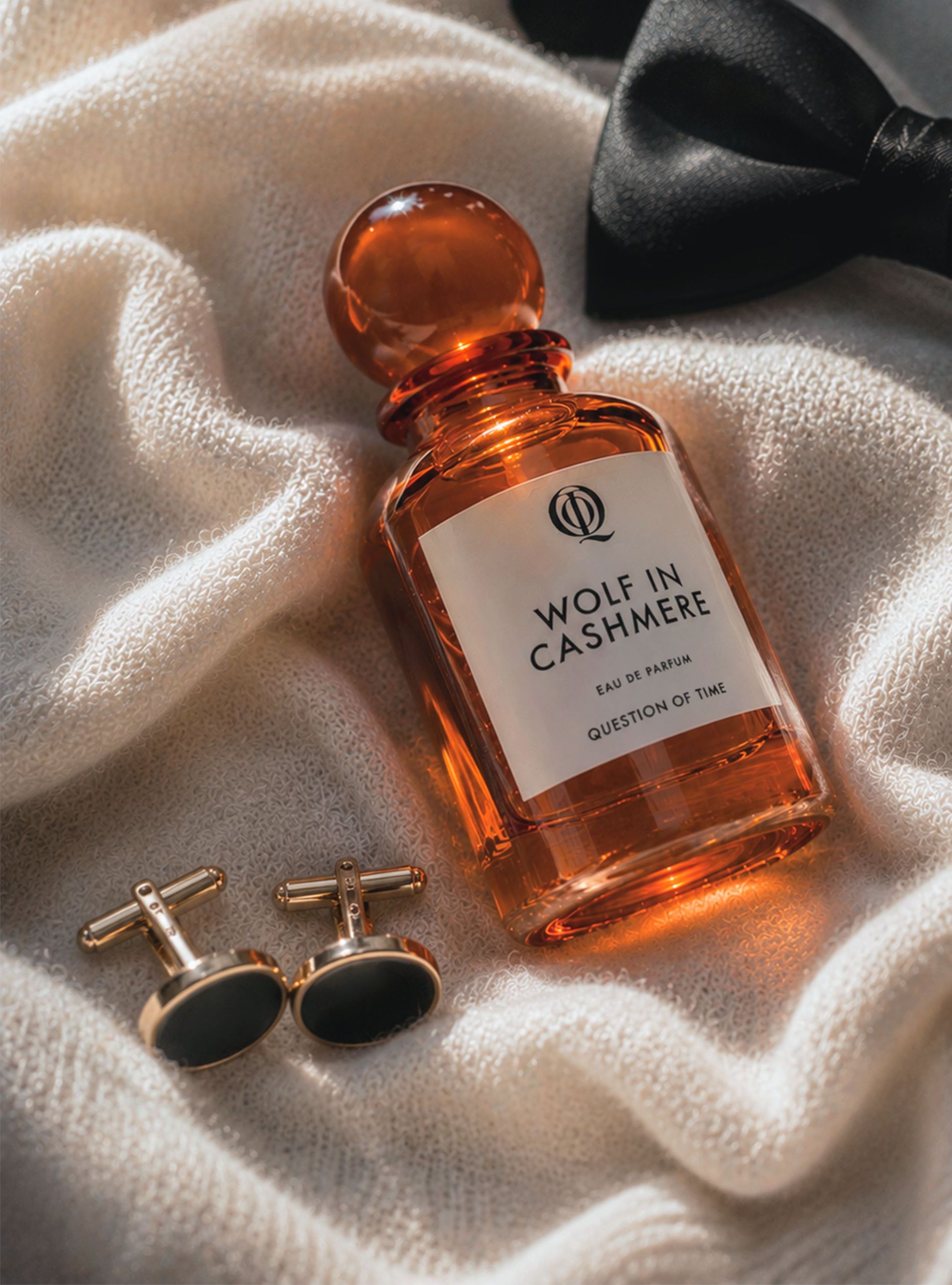 QOT's new scent Wolf In Cashmere displayed on a cashmere sweater with cufflinks and a bowtie