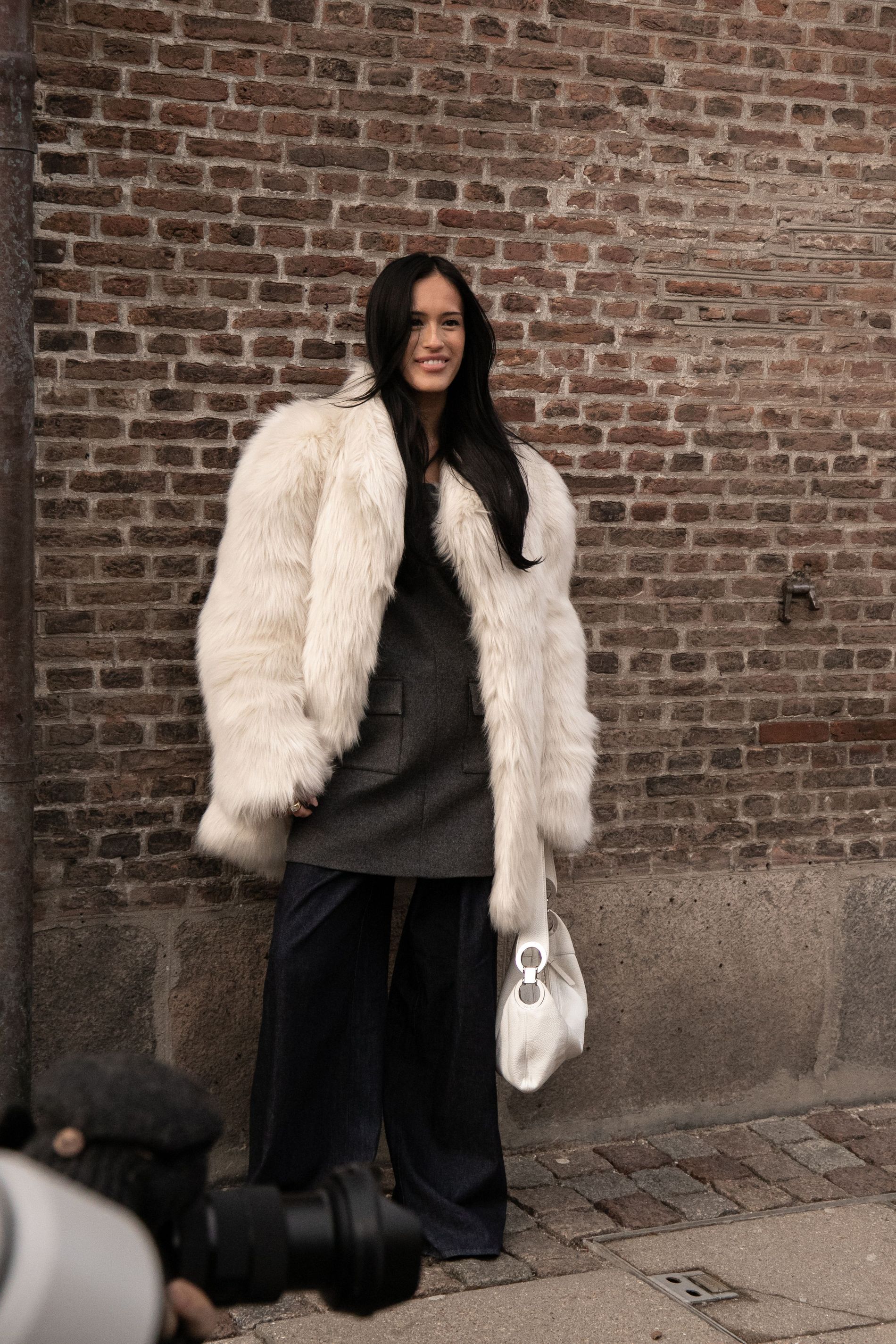 A CPHFW guest wears a white faux fur jacket with a grey dress and wide trousers while posing for street style
