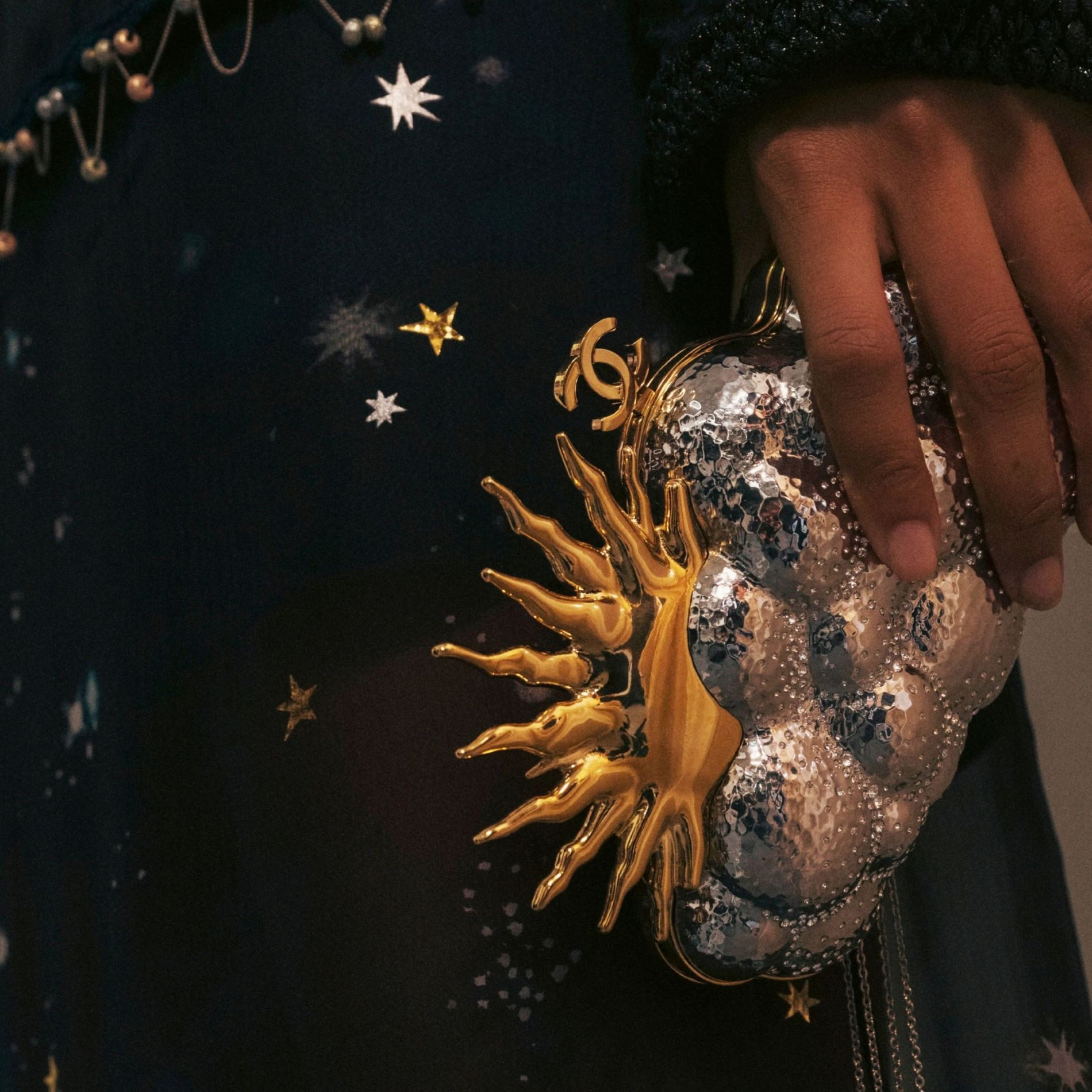 A close-up of a Chanel SS27 clutch in gold and silver, shaped like a cloud and sun
