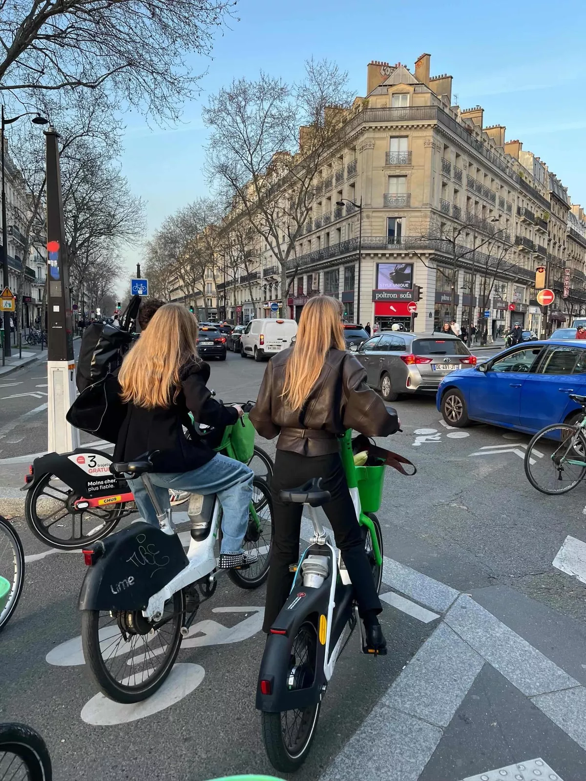 Two women on rented bicycles wait at a crossroad in Paris