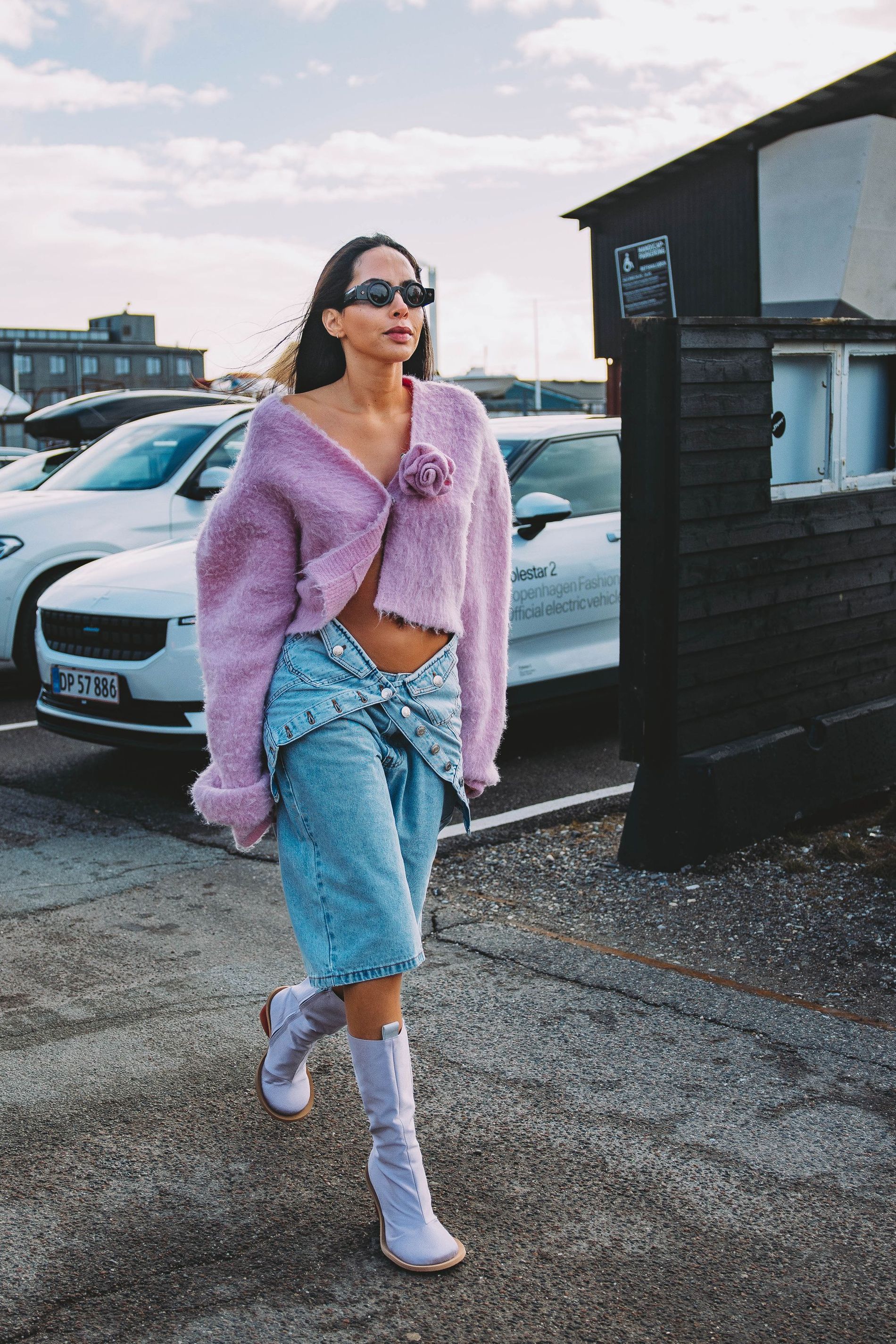 A guest at CPHFW poses for a street style photo wearing a lilac fuzzy cardigan with a fabric rose and a denim skirt