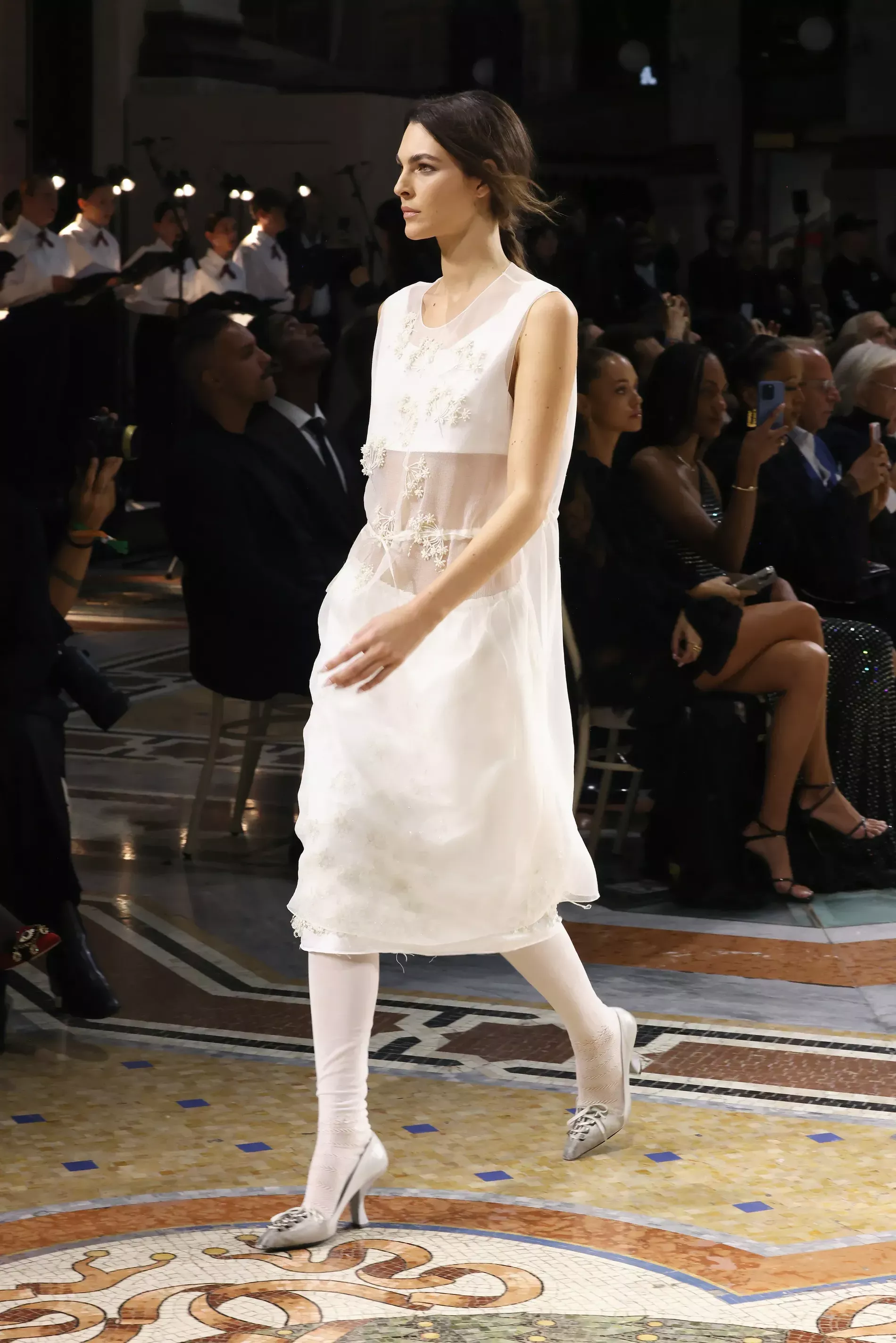 Vittoria Ceretti walking in Milan fashion week wearing a white transparent dress with pantyhose with grey Prada heels