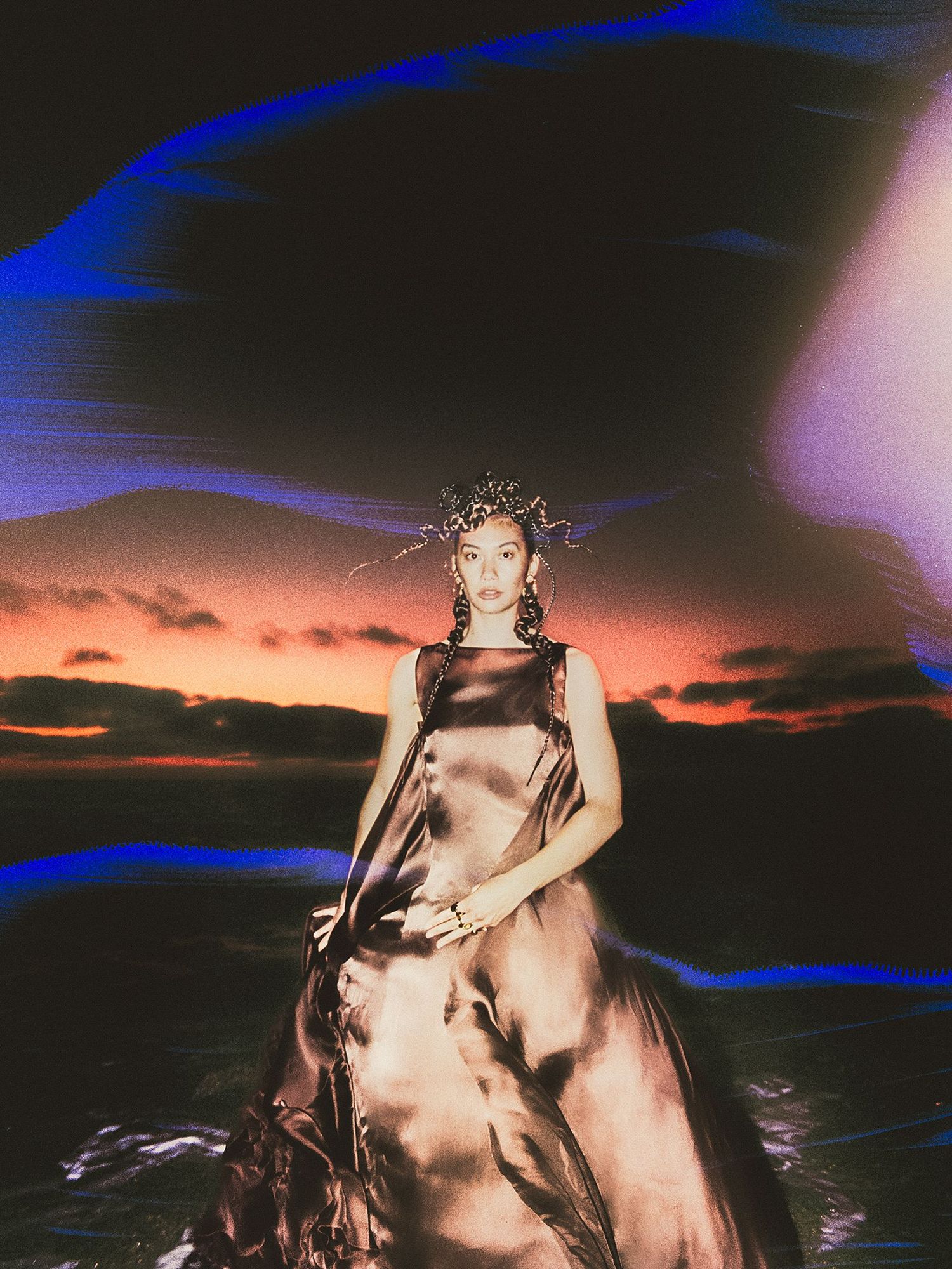 Model in satin dress stands outside with aurora above her