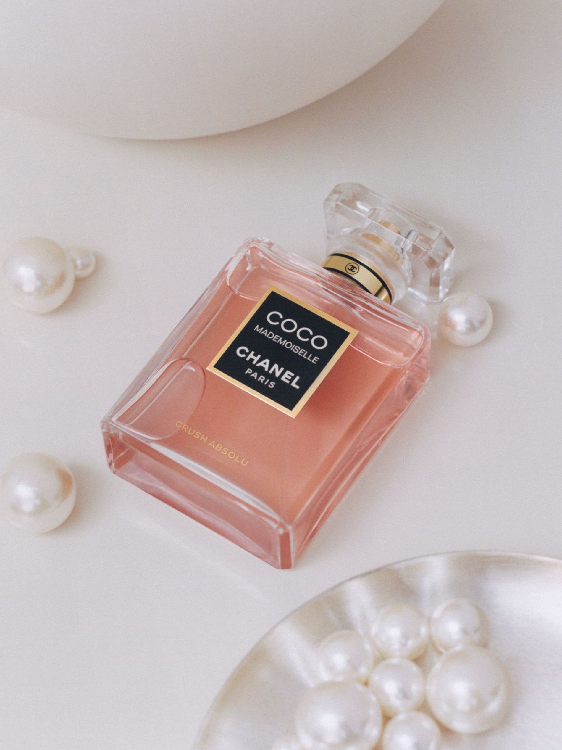 A bottle of Coco Madmoiselle Crush Absolu rests on a table with white pearls