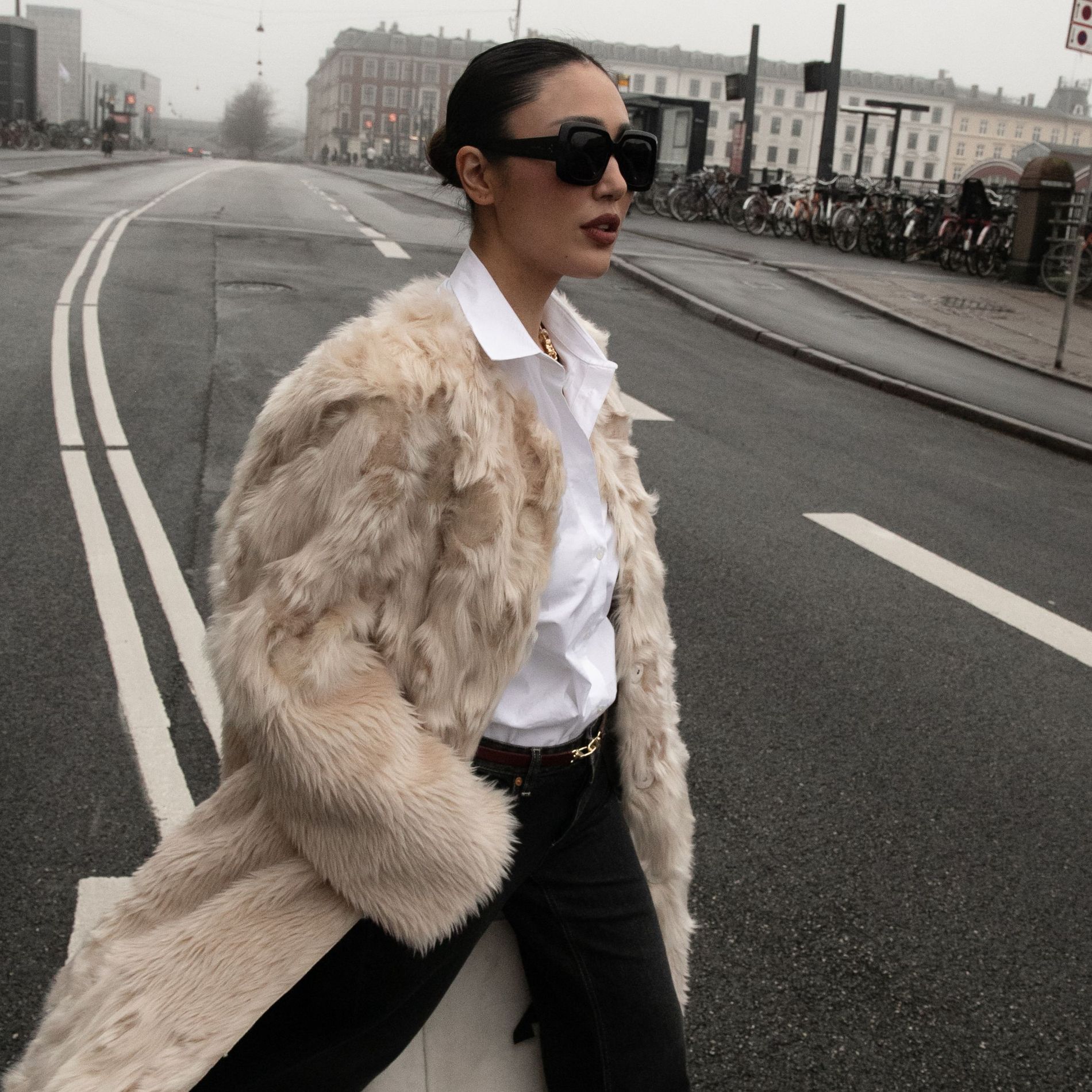A guest at Copenhagen Fashion Week wears a cream floor-length faux fur while posing for a street style image