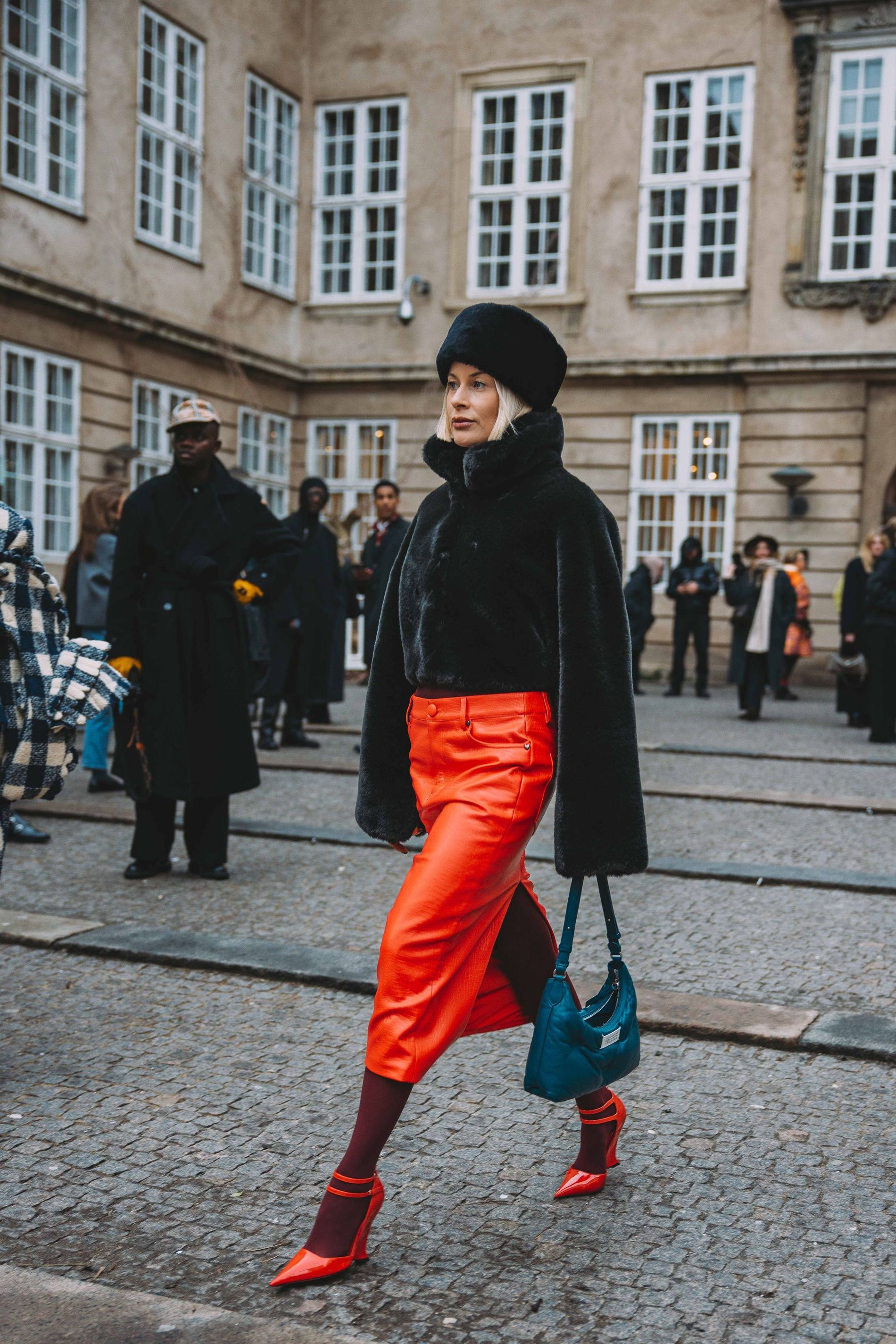 A guest at CPHFW poses for a street style image wearing a red skirt, burgundy stockings and red heels