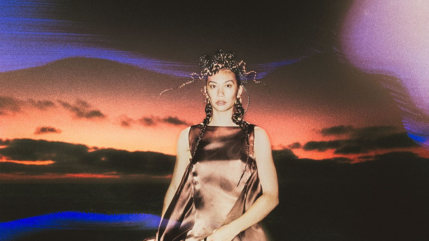 Model in satin dress stands outside with aurora above her