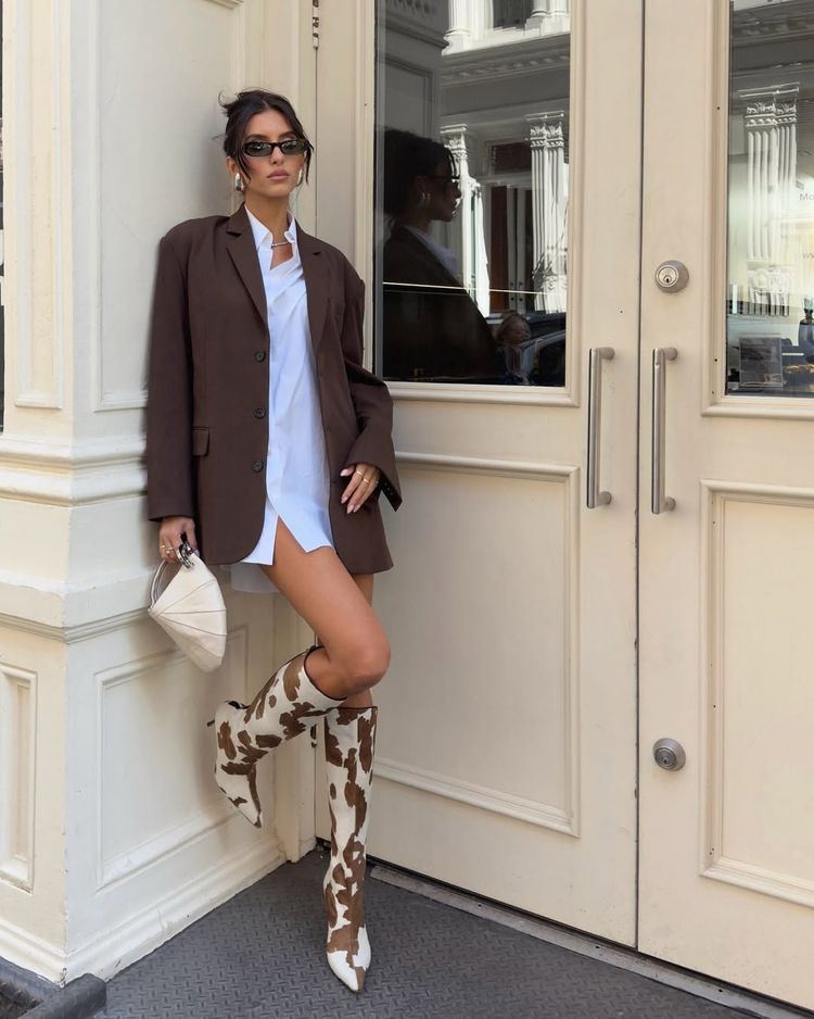 Street style photo of Christina Elezaj wearing knee-high cow print boots with an oversized blazer and shirtdress