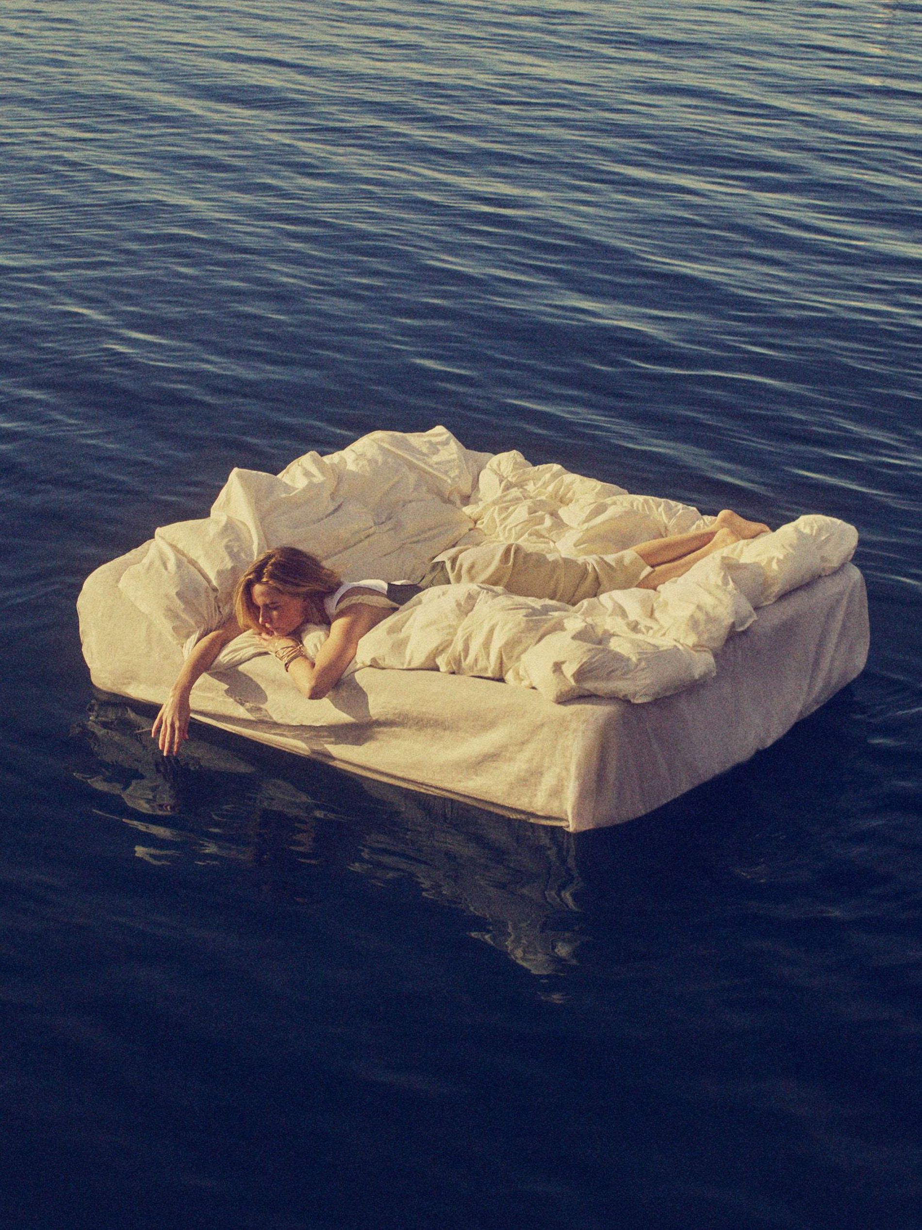 Rebecca Fergusson floats at sea on a mattress. She lies on a white fluffy duvet