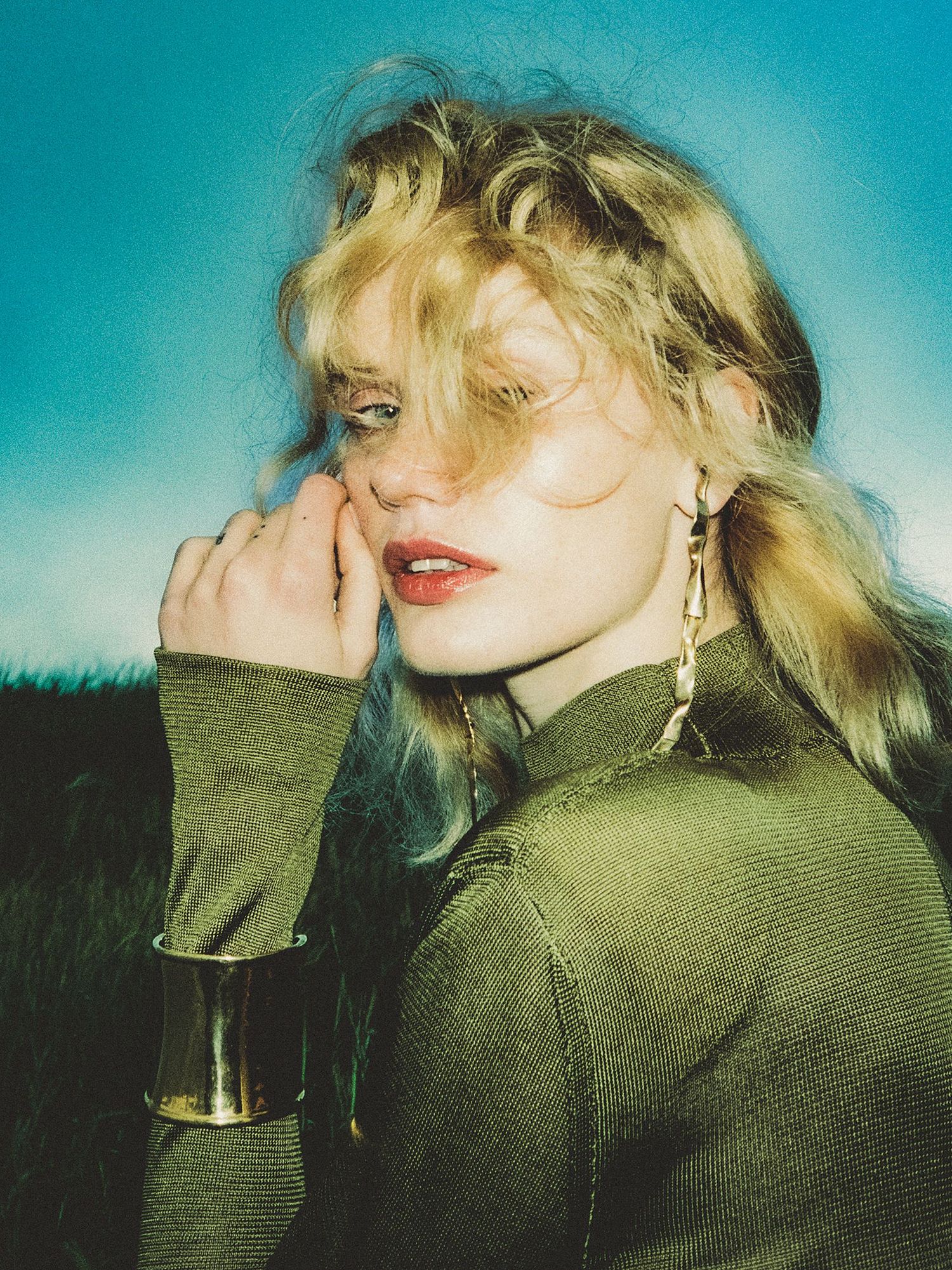 Model with tousled blonde hair and glowing skin looks at the camera framed by the setting summer sun