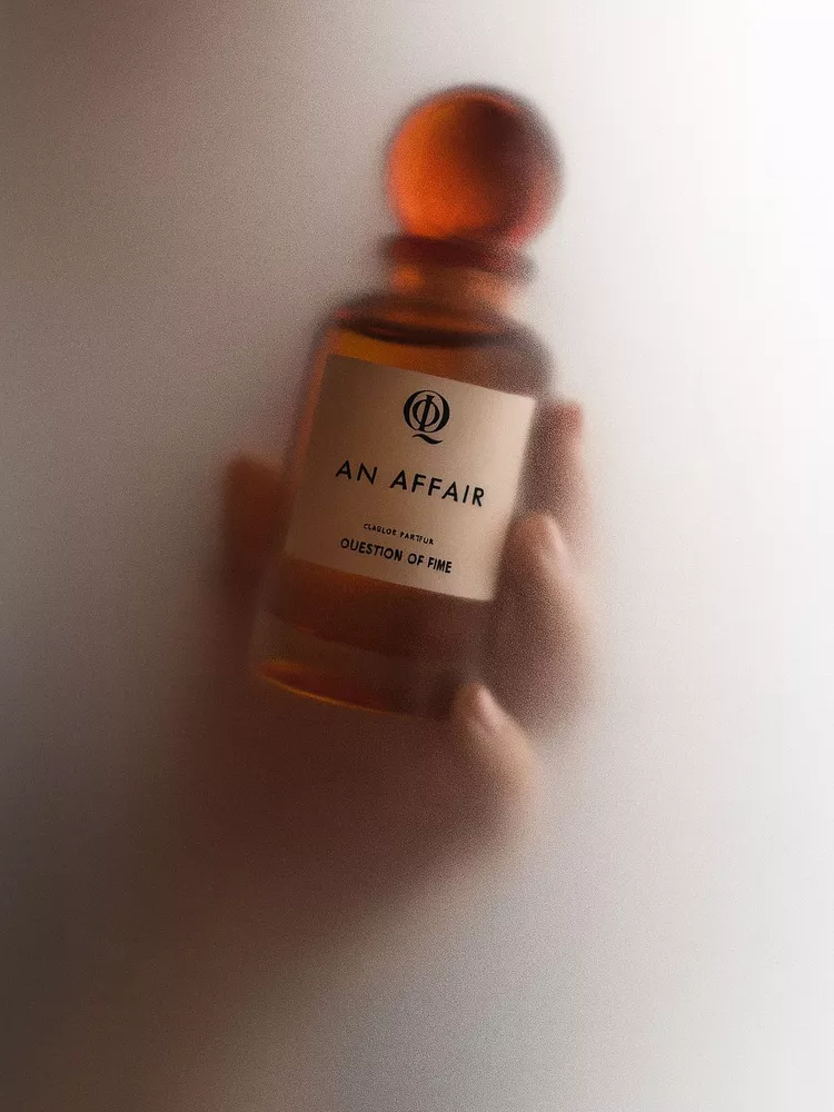 QOT's perfume 'An Affair' held in hand and surrounded by steam