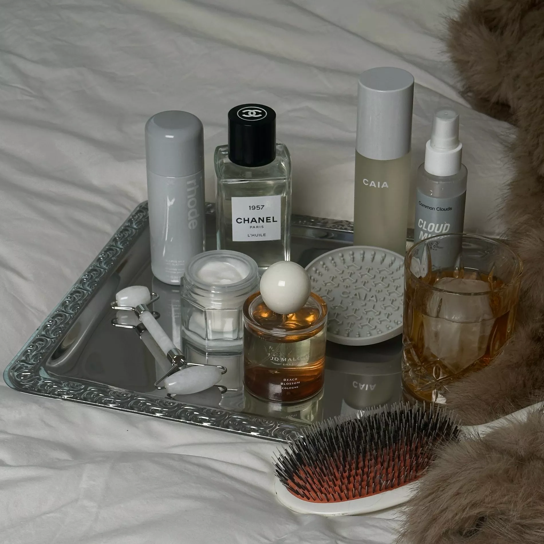 A collection of beauty items upon a silver tray on white sheets