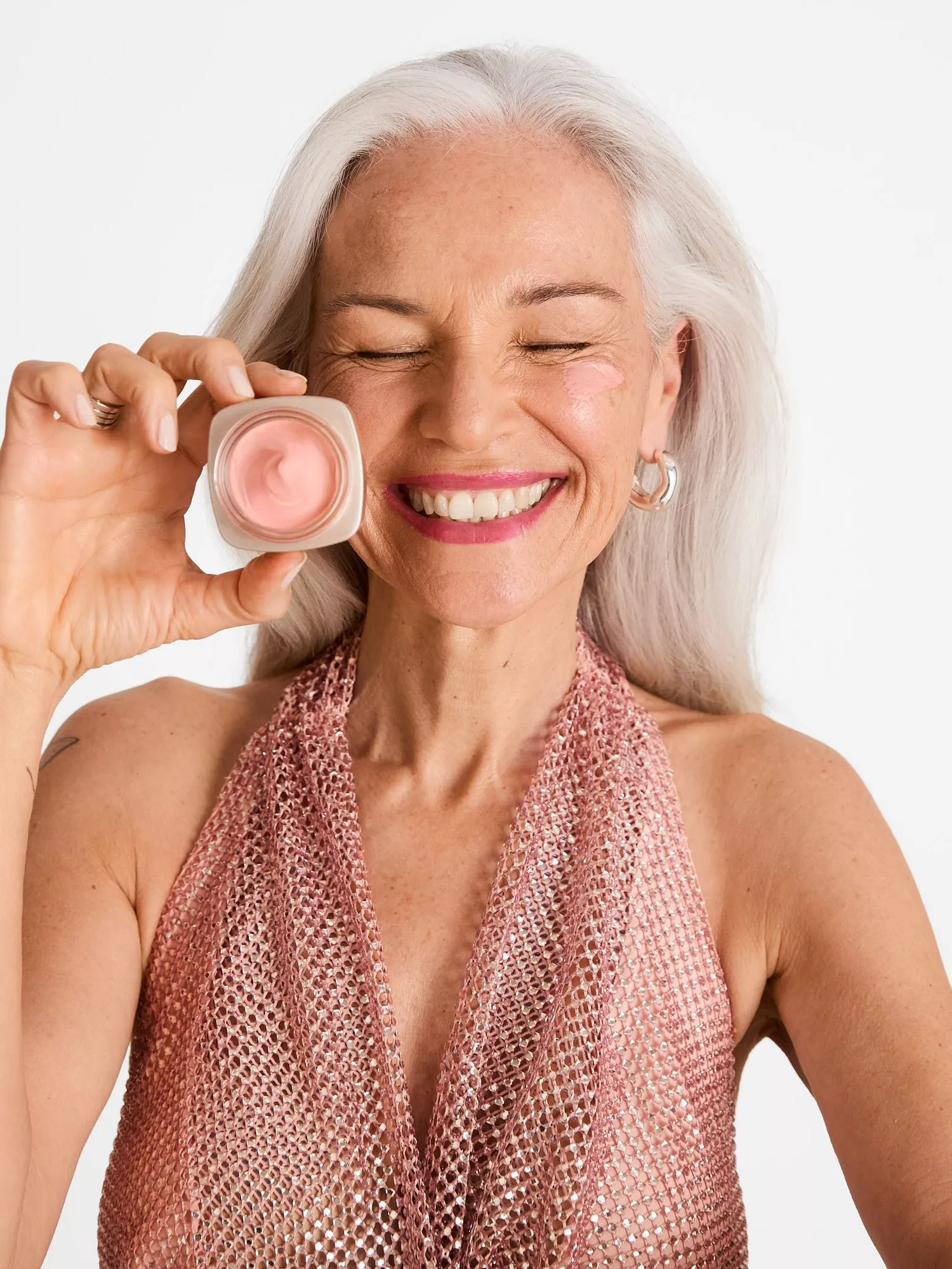 A mature model with white hair holds a rosy day cream 