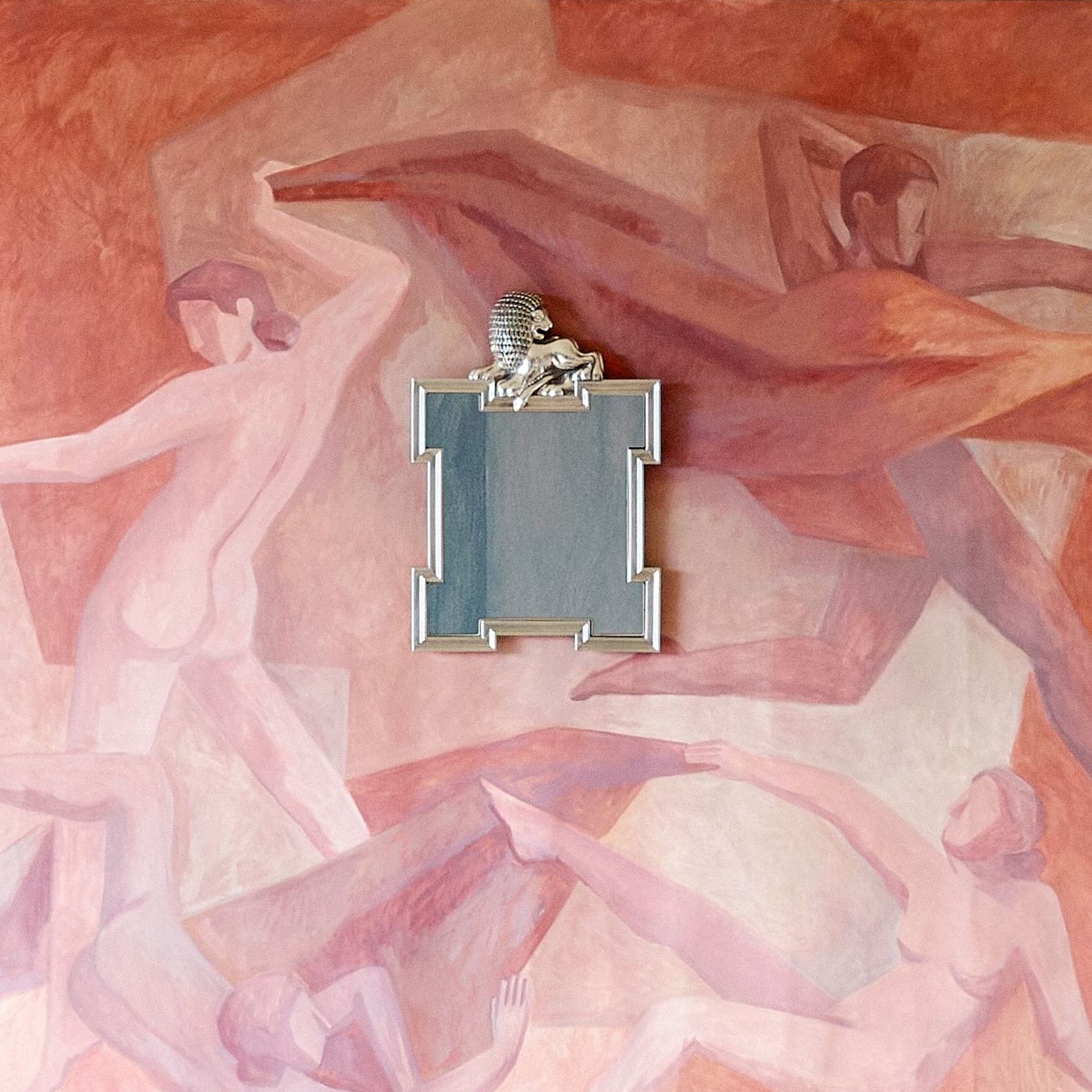 A red terracotta wall painted with naked people dancing and a silver mirror with a lion on the frame from Svenskt tenn Fall' 26