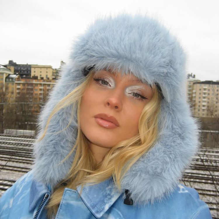 Zara Larsson wears a baby blue fuzzy hat and coat, paired with sparkling, frosty eyeshadow, nude lips and a sharp cat eye winged liner