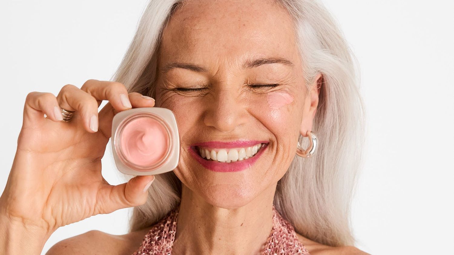 A mature model with white hair holds a rosy day cream