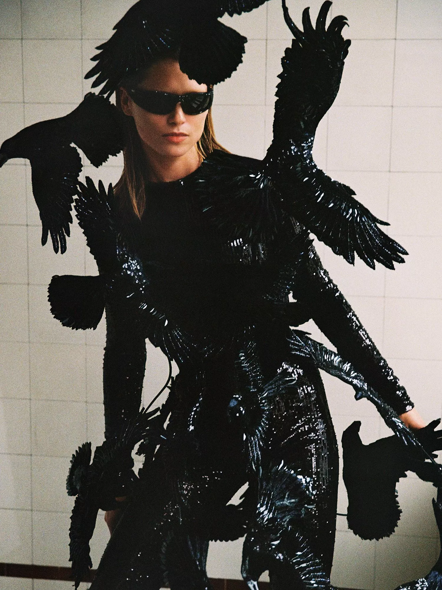 Model in black catsuit with crows in a white tiled room