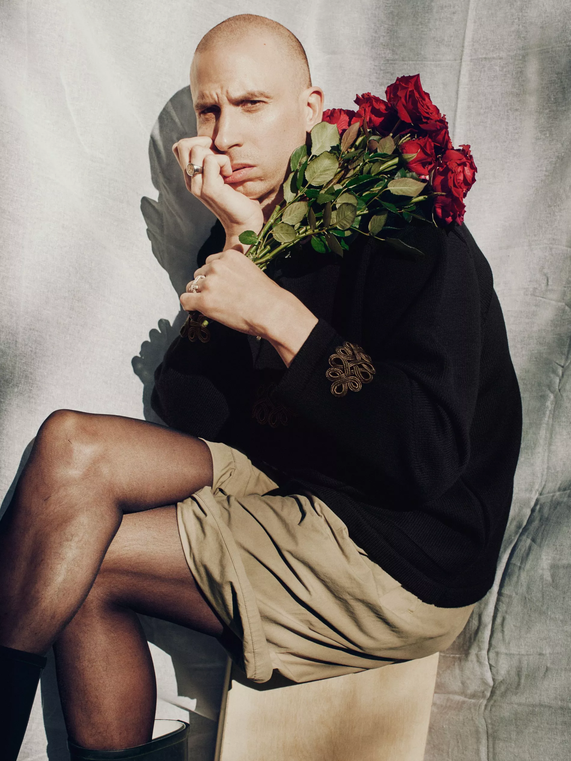Herbert is sitting holding roses and wearing a wool jacket with golden sleeve details and cotton capri shorts