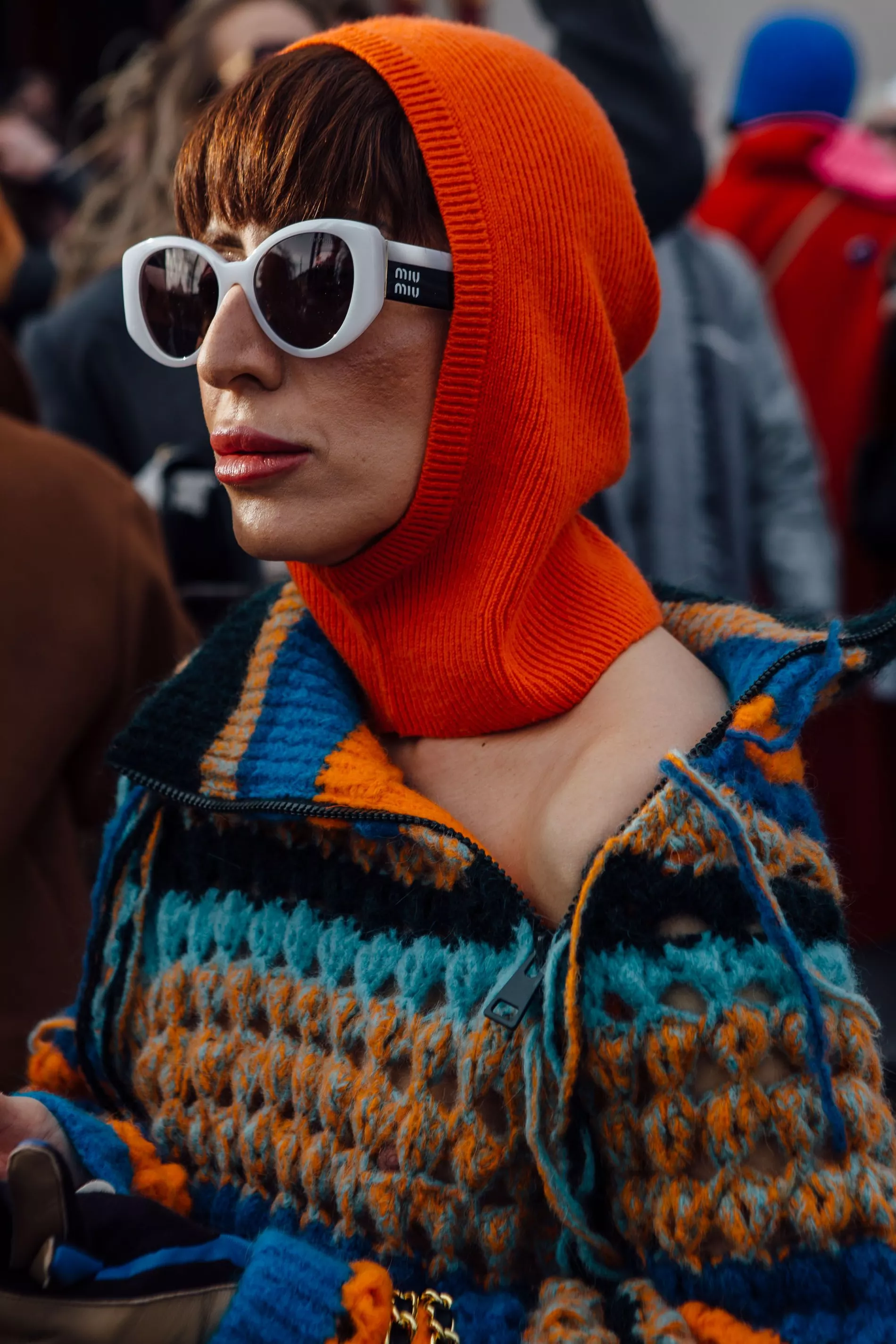 A guest wears Miu Miu sunglasses, an orange balaclava and a multi-coloured knitted top