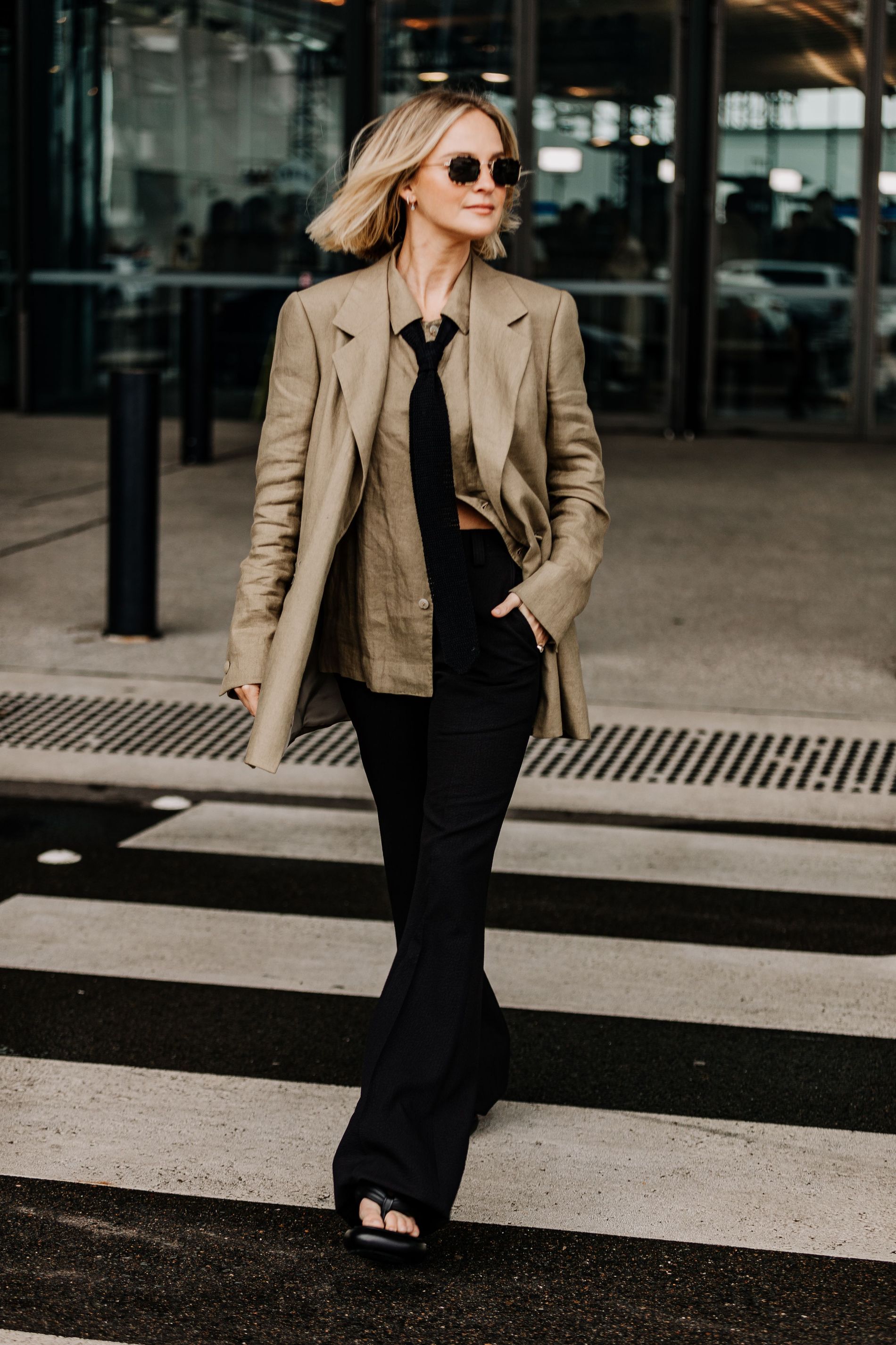 Woman wearing beige blazer and shirt with black necktie and trousers