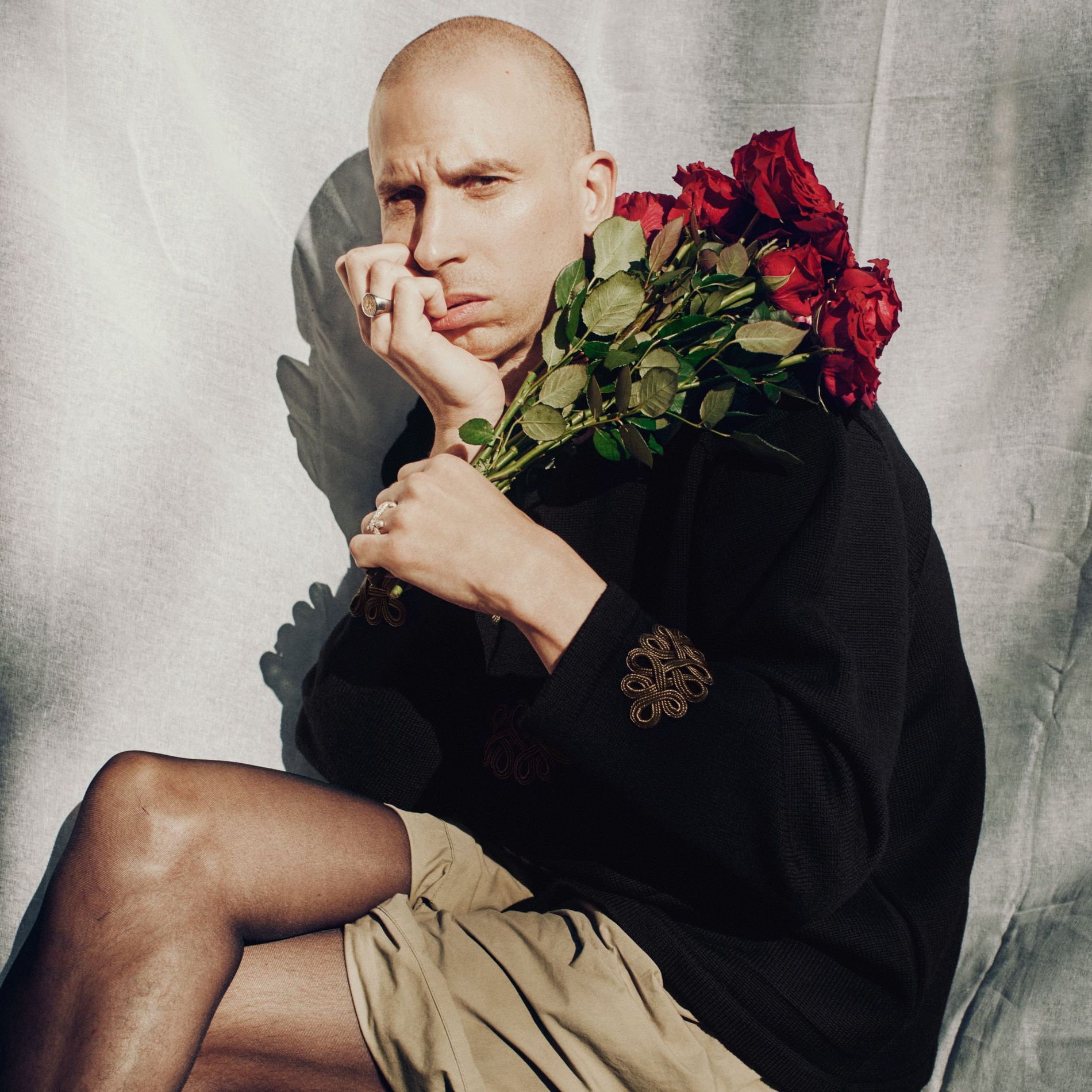 Herbert is sitting holding roses and wearing a wool jacket with golden sleeve details and cotton capri shorts