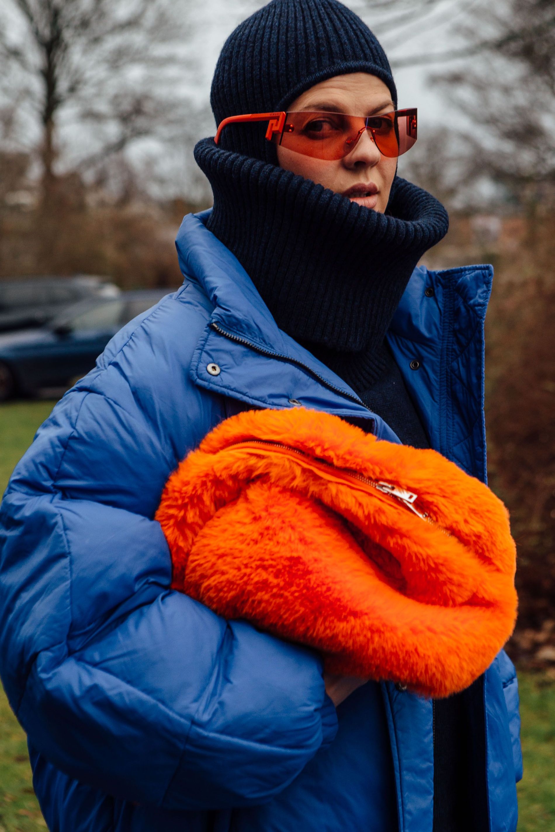 A street style CPHFW guest is captured wearing orange accessories, a trendy navy balaclava with a matching roll neck, and a light blue puffer