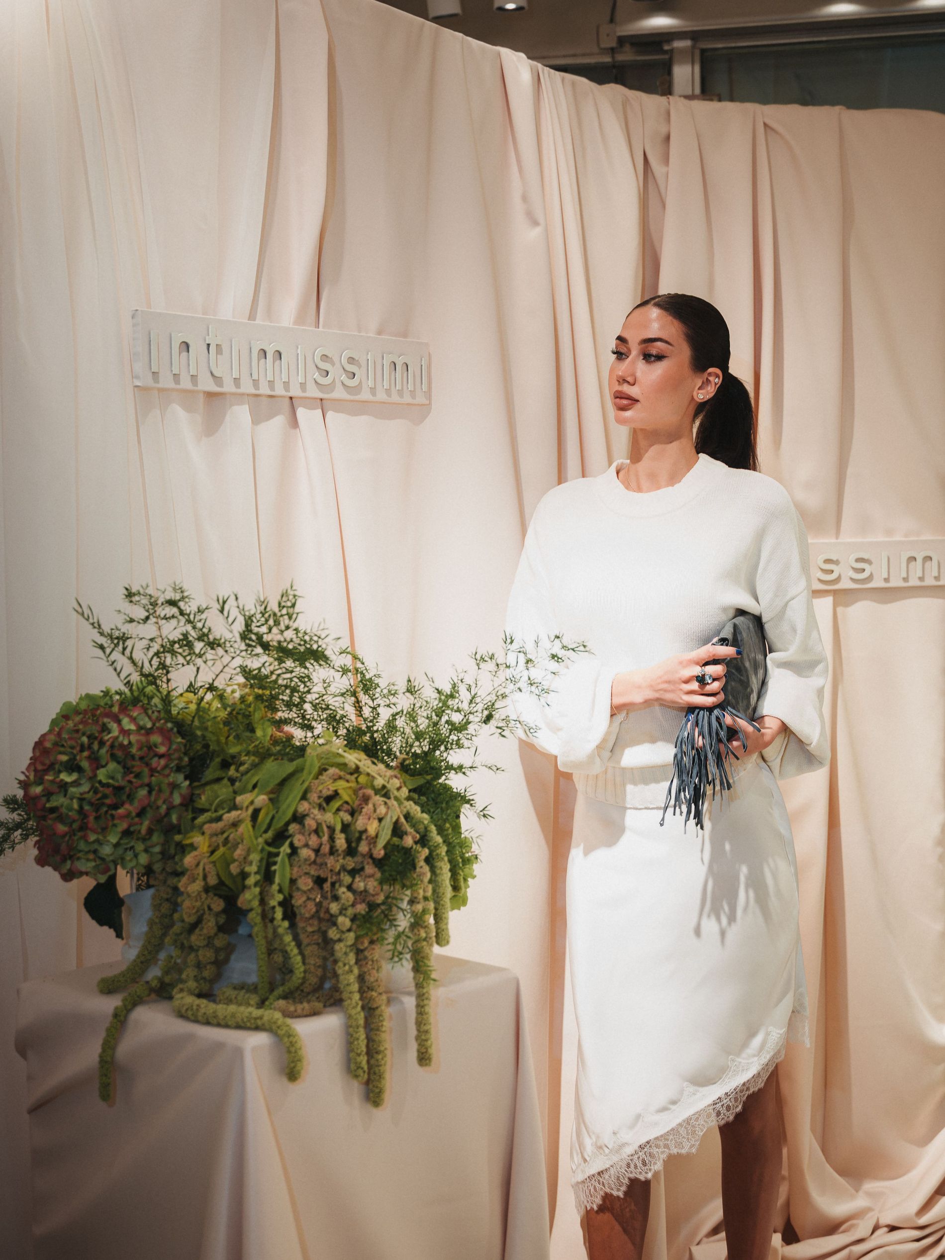 Girl posing in white clothing on the Intimissimi opening event, with a intimissimi background and a bouquet