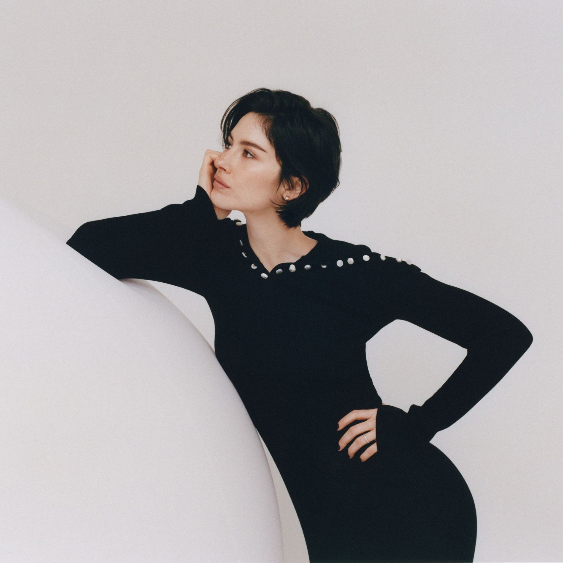 Gracie Abrams poses in a black knitted dress on a white soundstage for the Coco Mademoiselle Cursh Absolu campaign