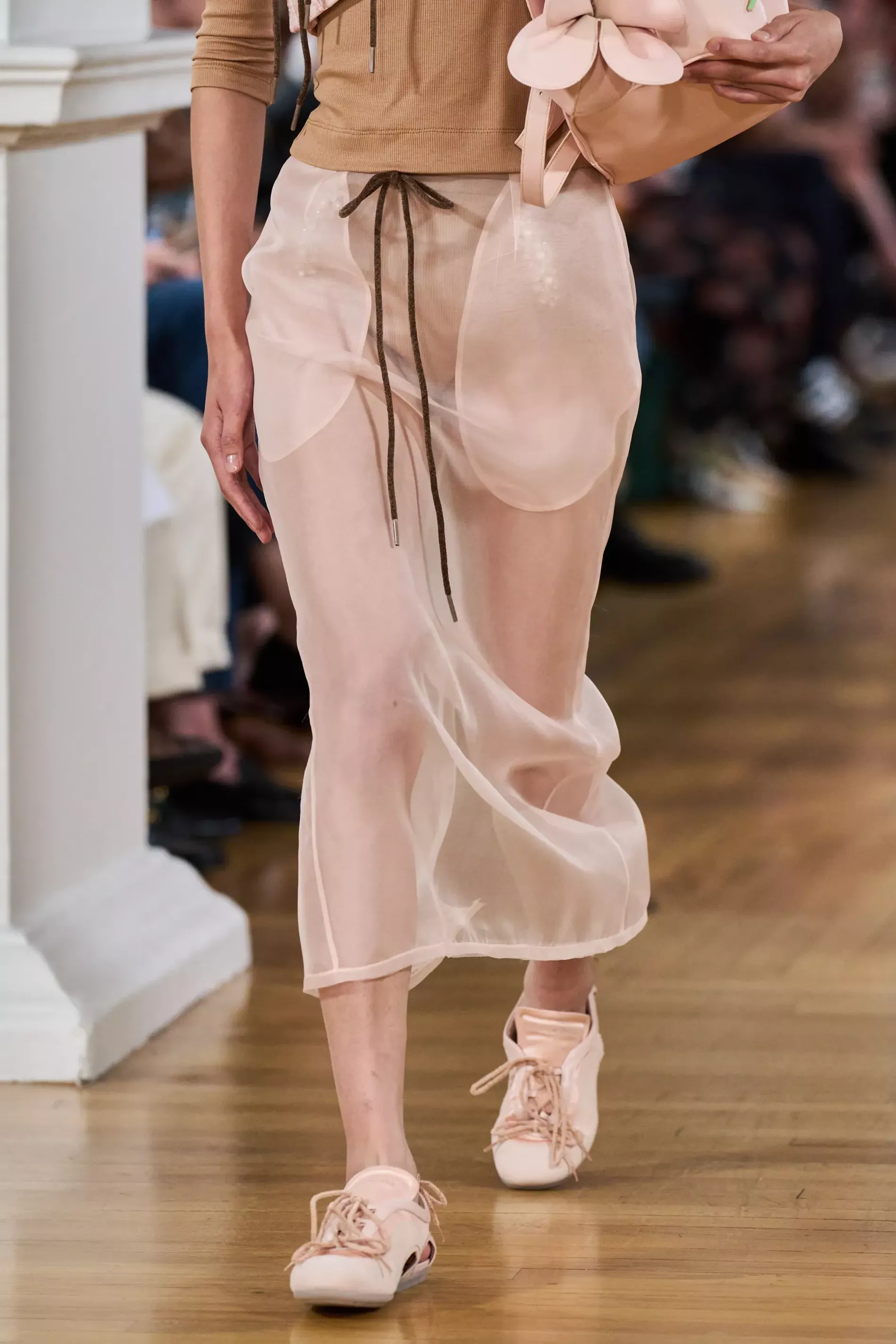 The lower half of a model walking Simone Rocha's spring/summer 2026 runway in a pale pink sheer skirt and matching sneakerinas