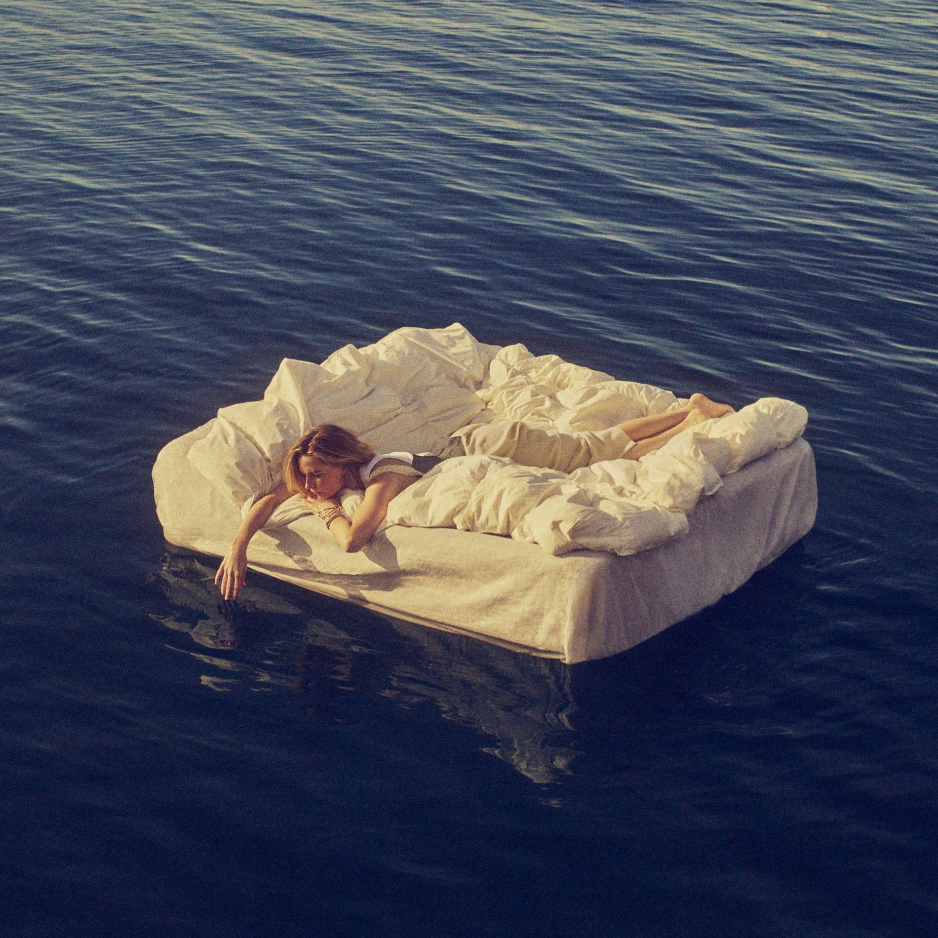 Rebecca Fergusson floats at sea on a mattress. She lies on a white fluffy duvet