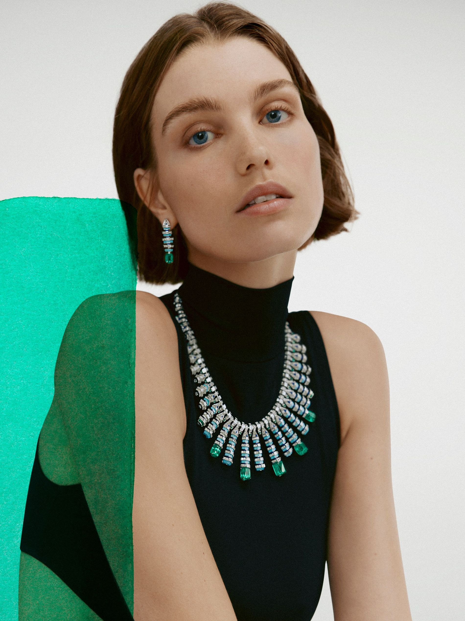 Model in black wears an earring and a necklace from Cartier high jewellery against a white background with a green swipe of paint